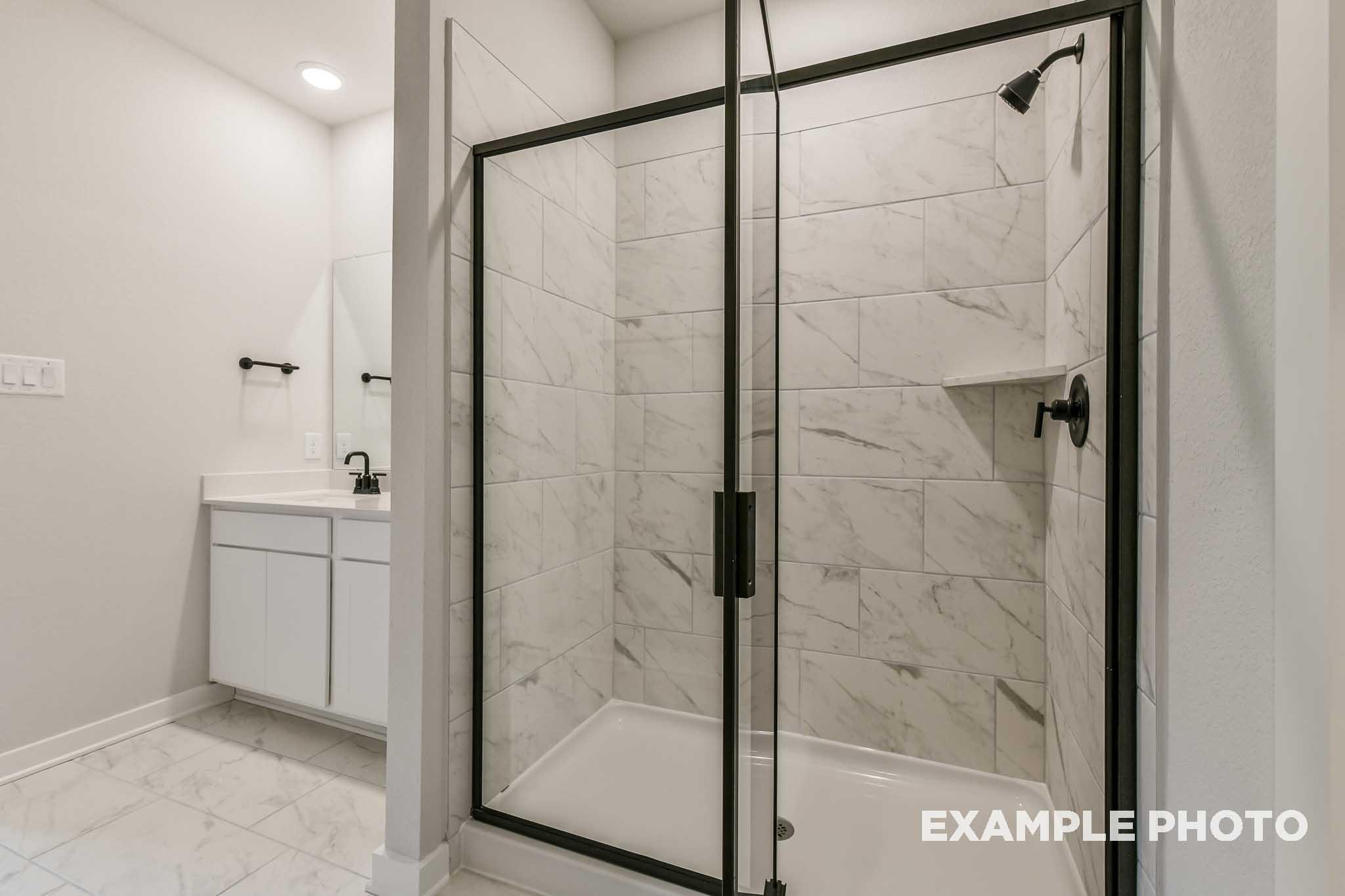 Spacious master bathroom in The Daphne G featuring frameless glass shower, white subway tile walls, and modern vanity