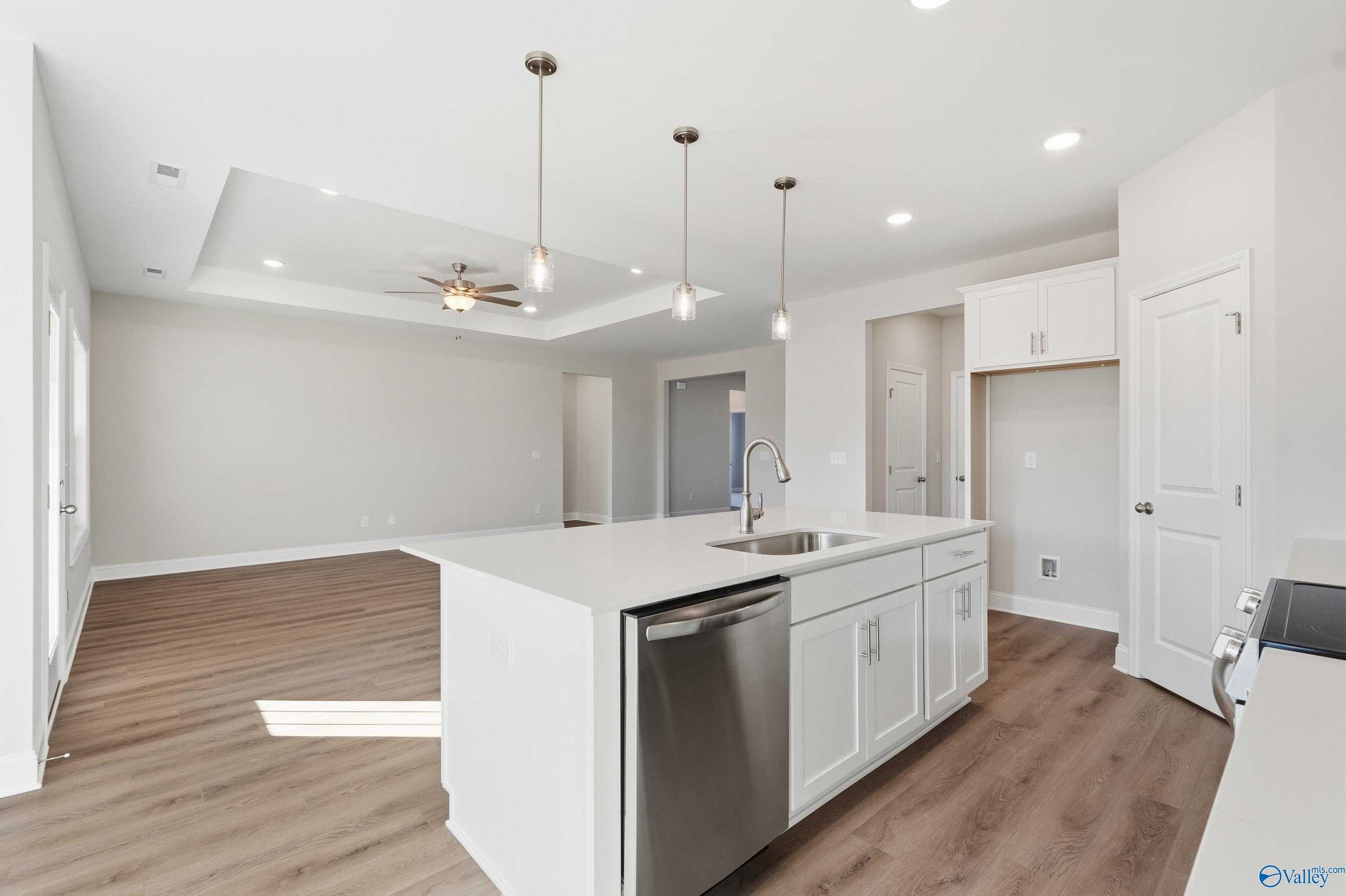 Modern open kitchen with white island, stainless dishwasher, pendant lights, and ceiling fan in Davidson Homes The Montgomery B, Toney, AL