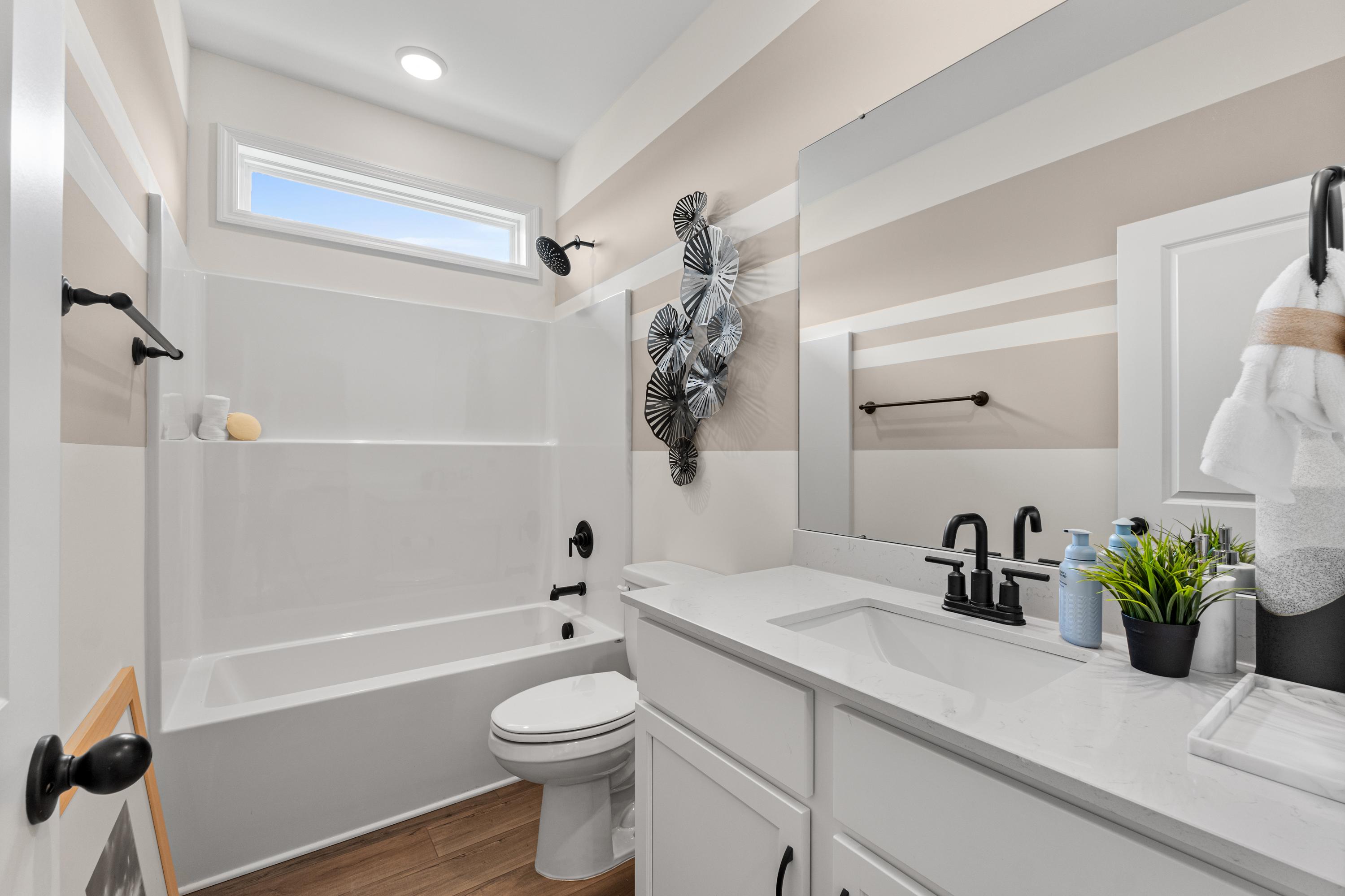 Bright bathroom in Lynn Meadows Meridianville Alabama with white subway tile tub-shower, quartz vanity, and seashell wall decor