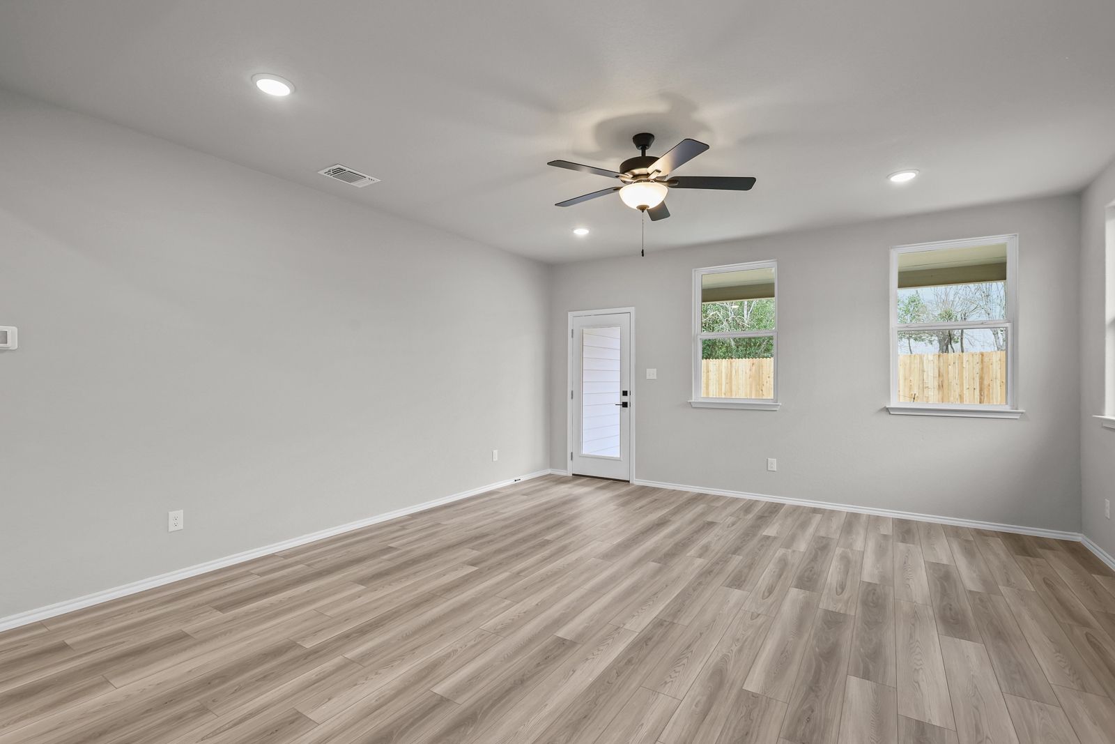 Spacious living area in The Glenwood featuring light gray walls, wood-look flooring, ceiling fan, and backyard access.