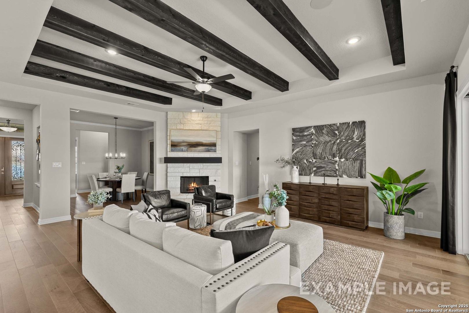 Cozy living room featuring white sectional sofa, stone fireplace, beamed ceiling, and open dining in Davidson Homes The Summerlin B, Castroville, Texas