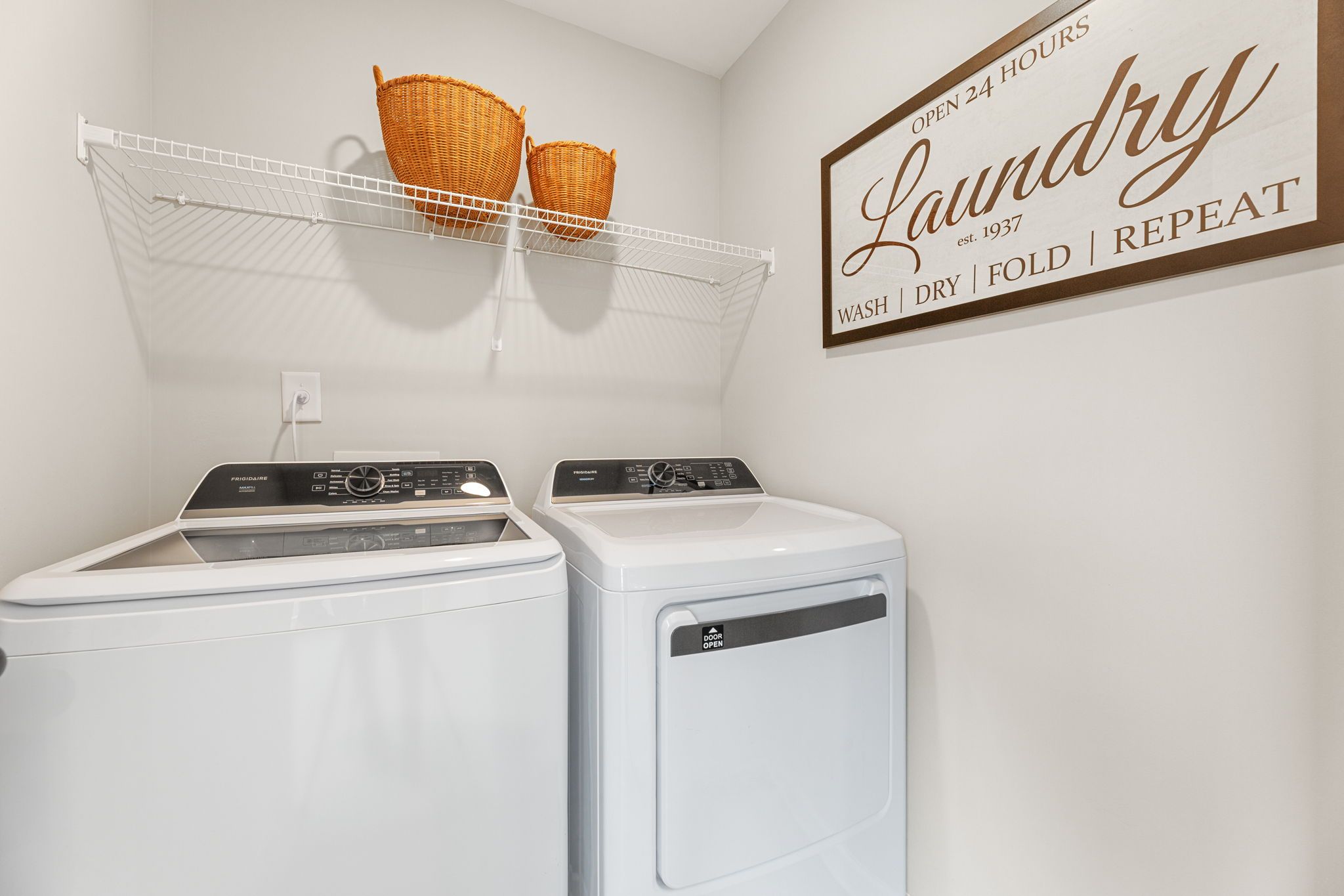 Functional laundry room featuring Frigidaire washer dryer, wire shelving with wicker baskets, and rustic sign in Davidson Homes The Durham B, Cumming, GA