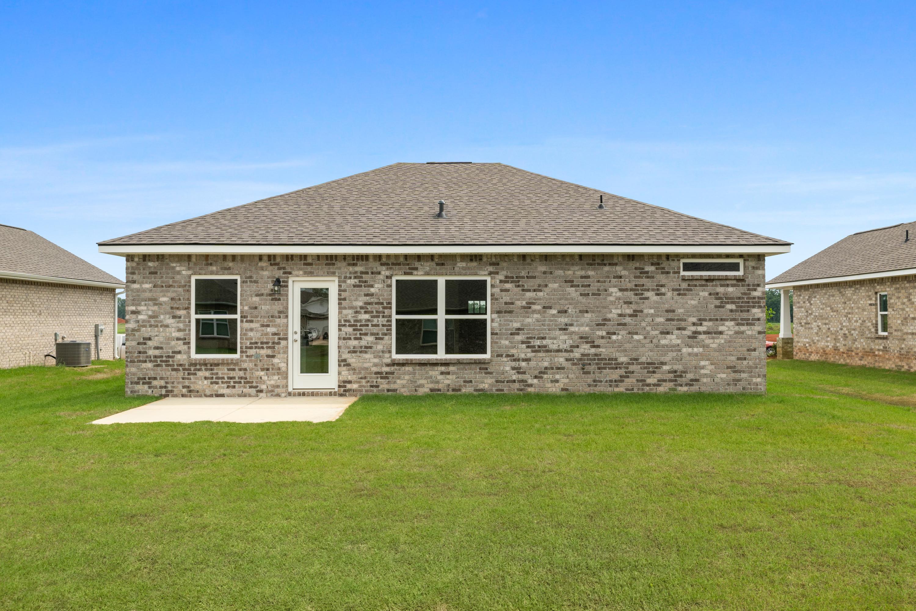 Rear elevation of The Butler single-story home featuring brick exterior, large windows, patio door, and green lawn in Meridianville