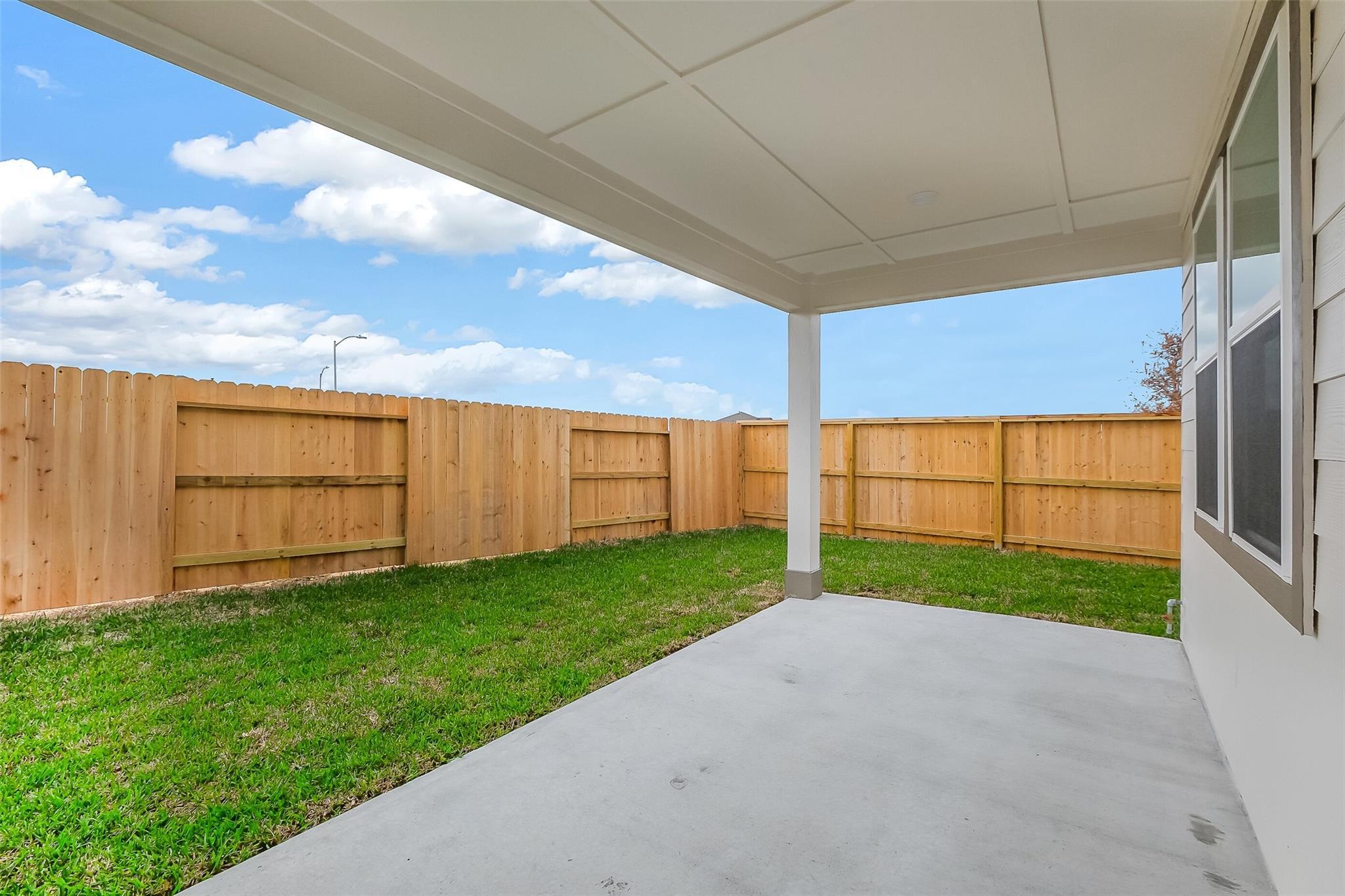Covered patio with concrete slab overlooking fenced grassy backyard under blue sky in Davidson Homes The Tierra B, Beasley, Texas
