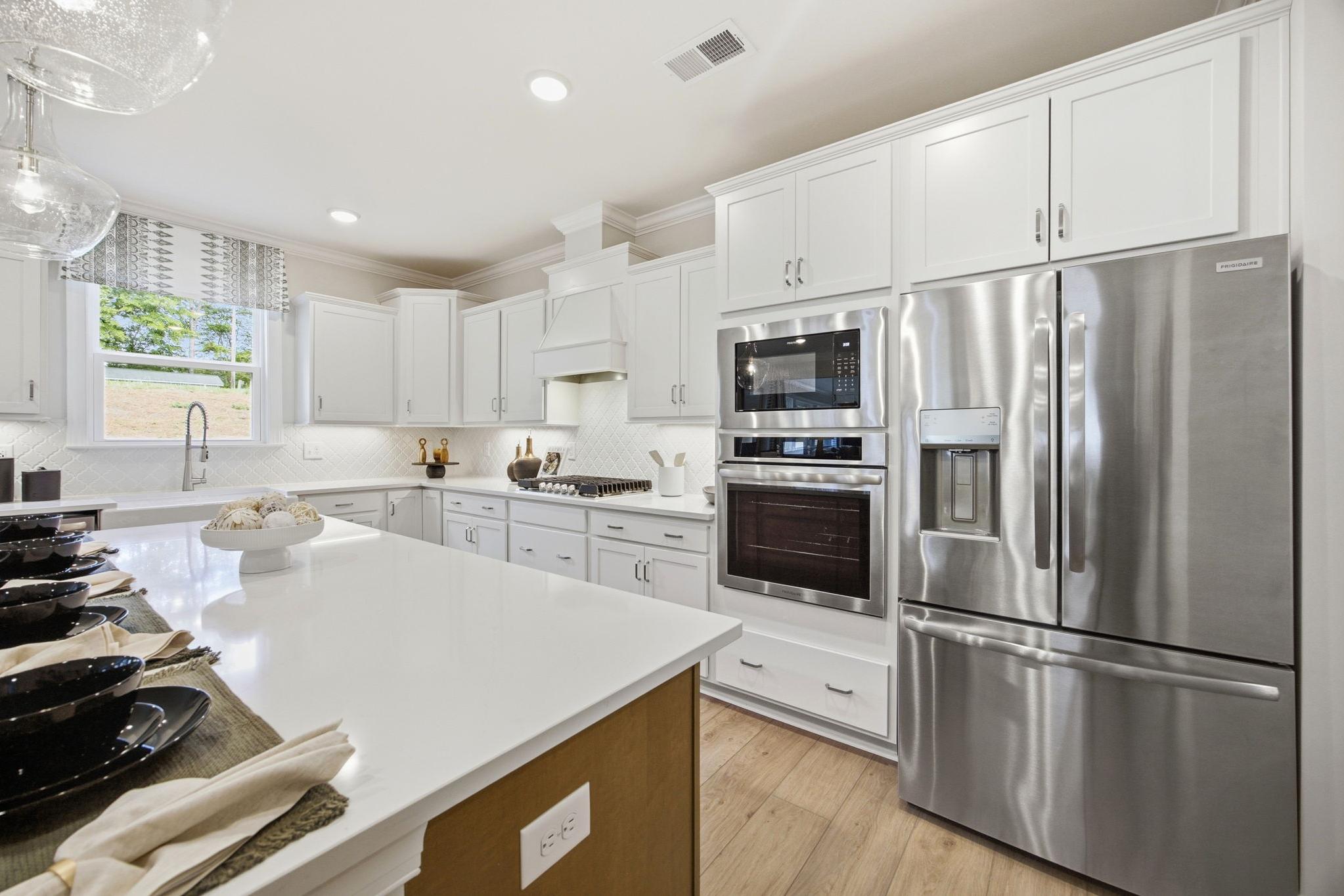 Modern white kitchen at Enclave at Belmont in Belmont NC featuring stainless steel Frigidaire appliances, quartz island and hardwood floors