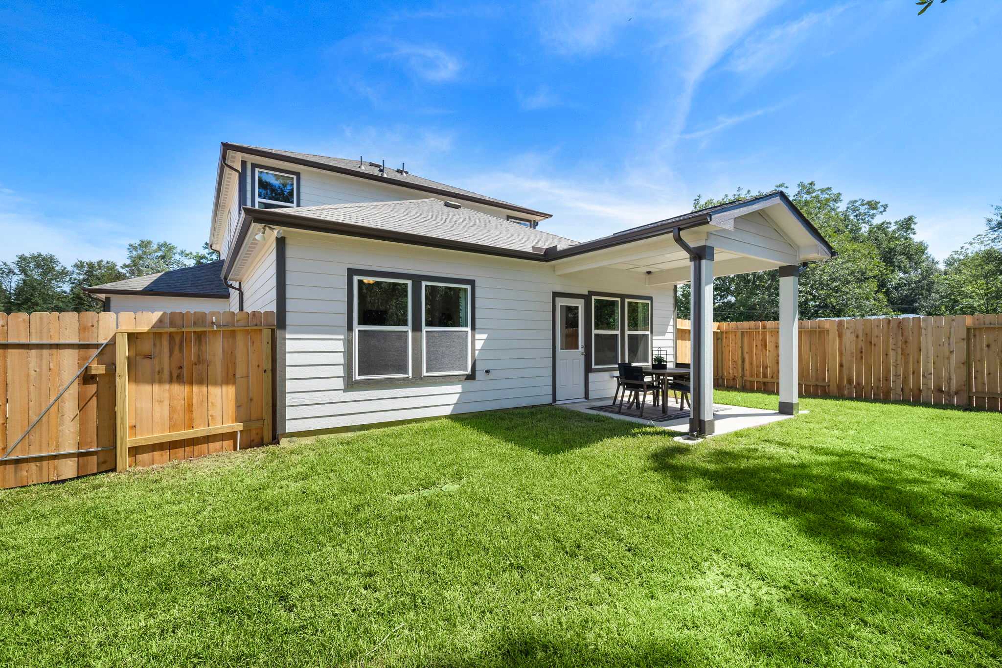 Covered backyard patio at Caney Creek Place in Conroe TX with seating, lush green lawn, and wooden fence