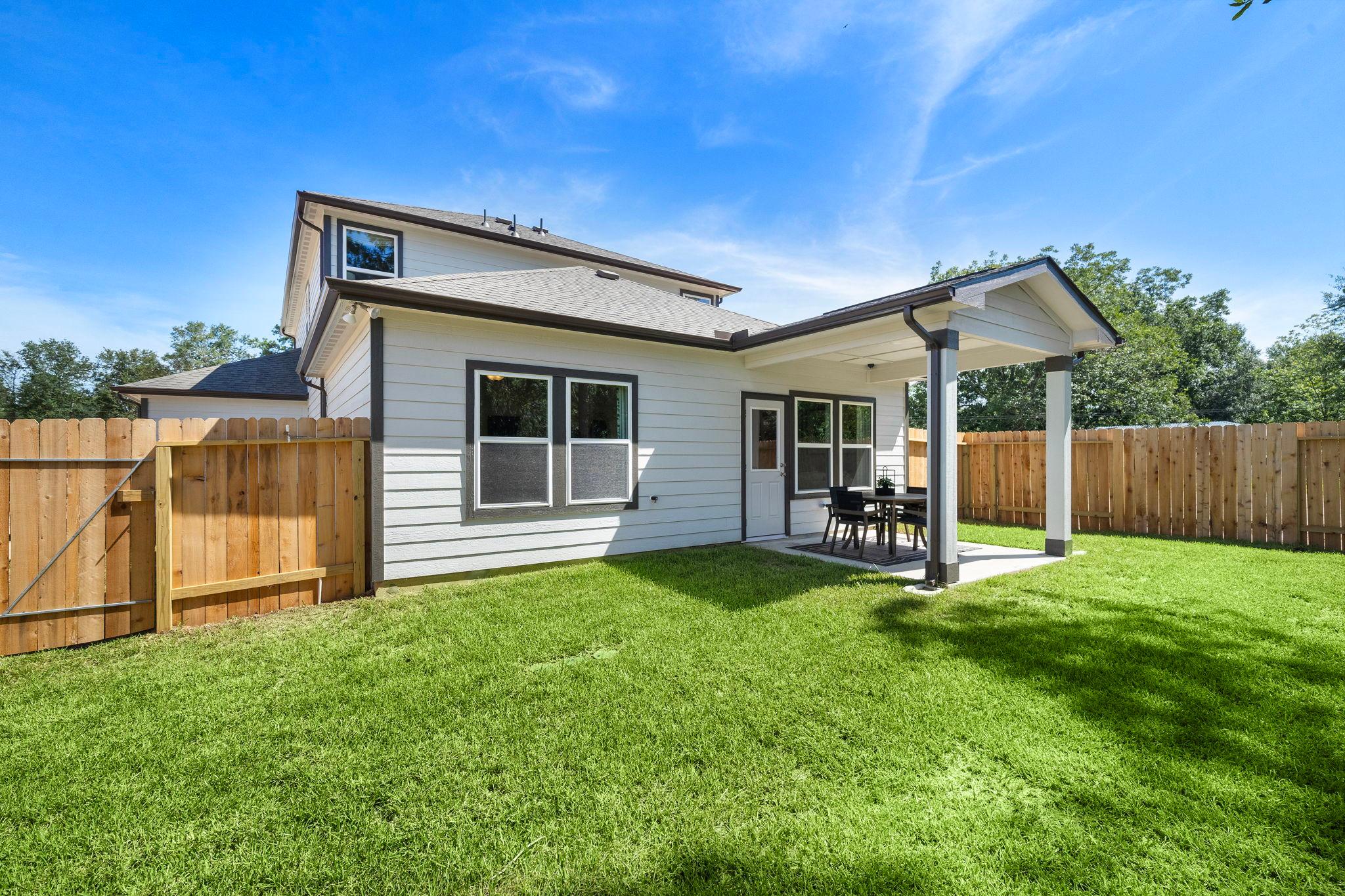 Covered backyard patio at Caney Creek Place in Conroe TX with seating, lush green lawn, and wooden fence