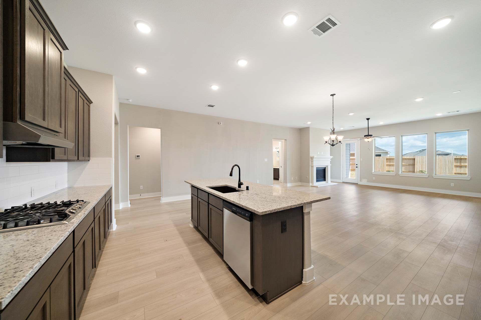 Open-concept kitchen and living area in The Elizabeth by Davidson Homes, featuring granite island, dark cabinetry, and fireplace.