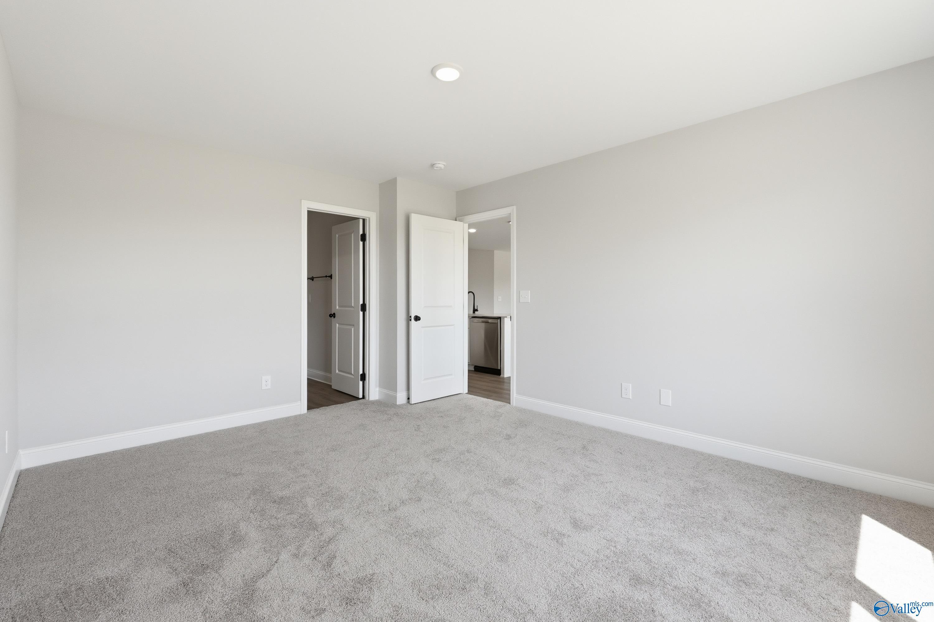 Empty bedroom with gray carpet, white walls, and doors to bathroom and closet in Davidson Homes The Franklin V, Athens, Alabama