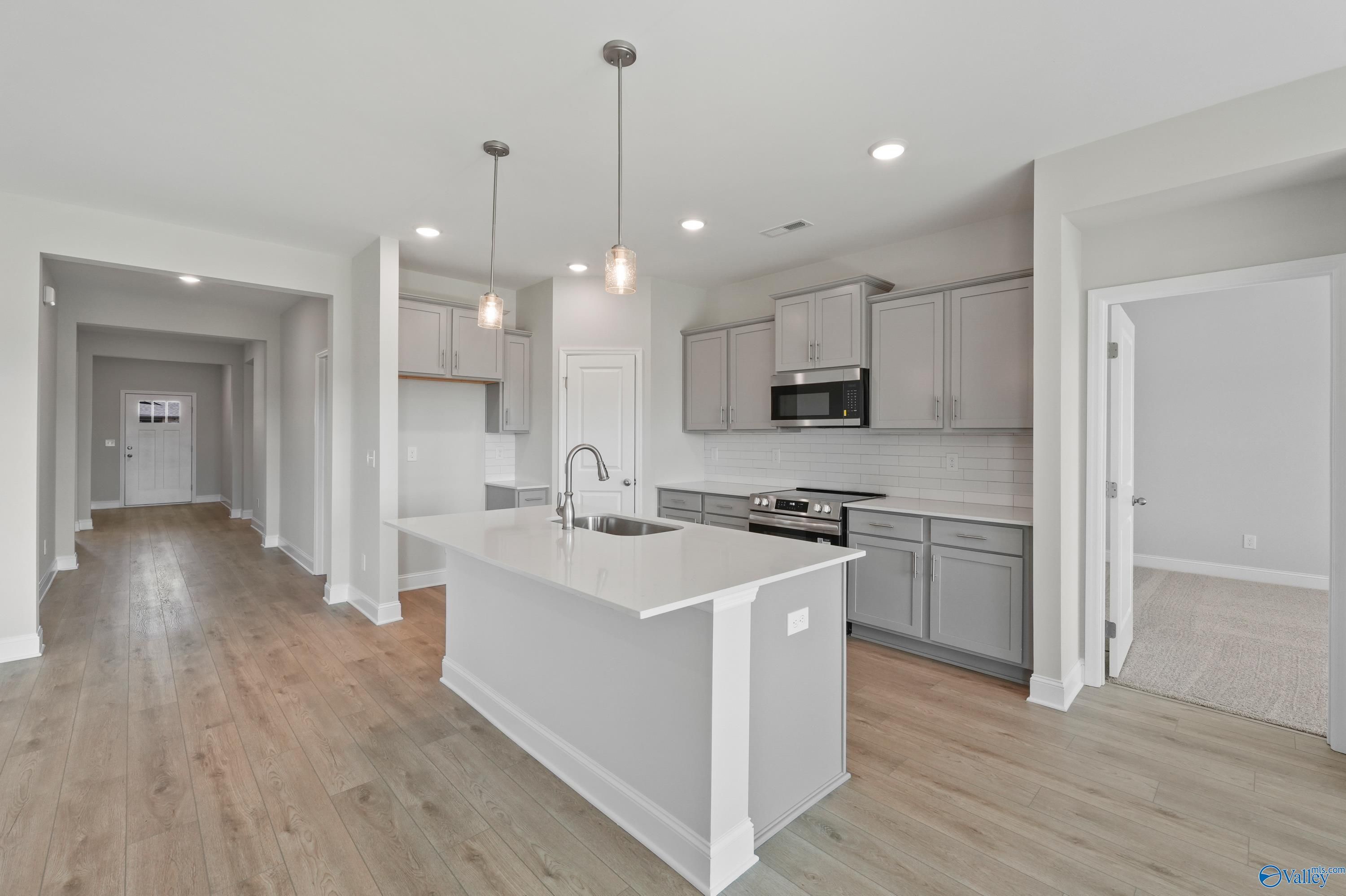 Modern open-concept kitchen featuring white island, stainless appliances, and hardwood floors in The Everett by Davidson Homes, Hazel Green, AL