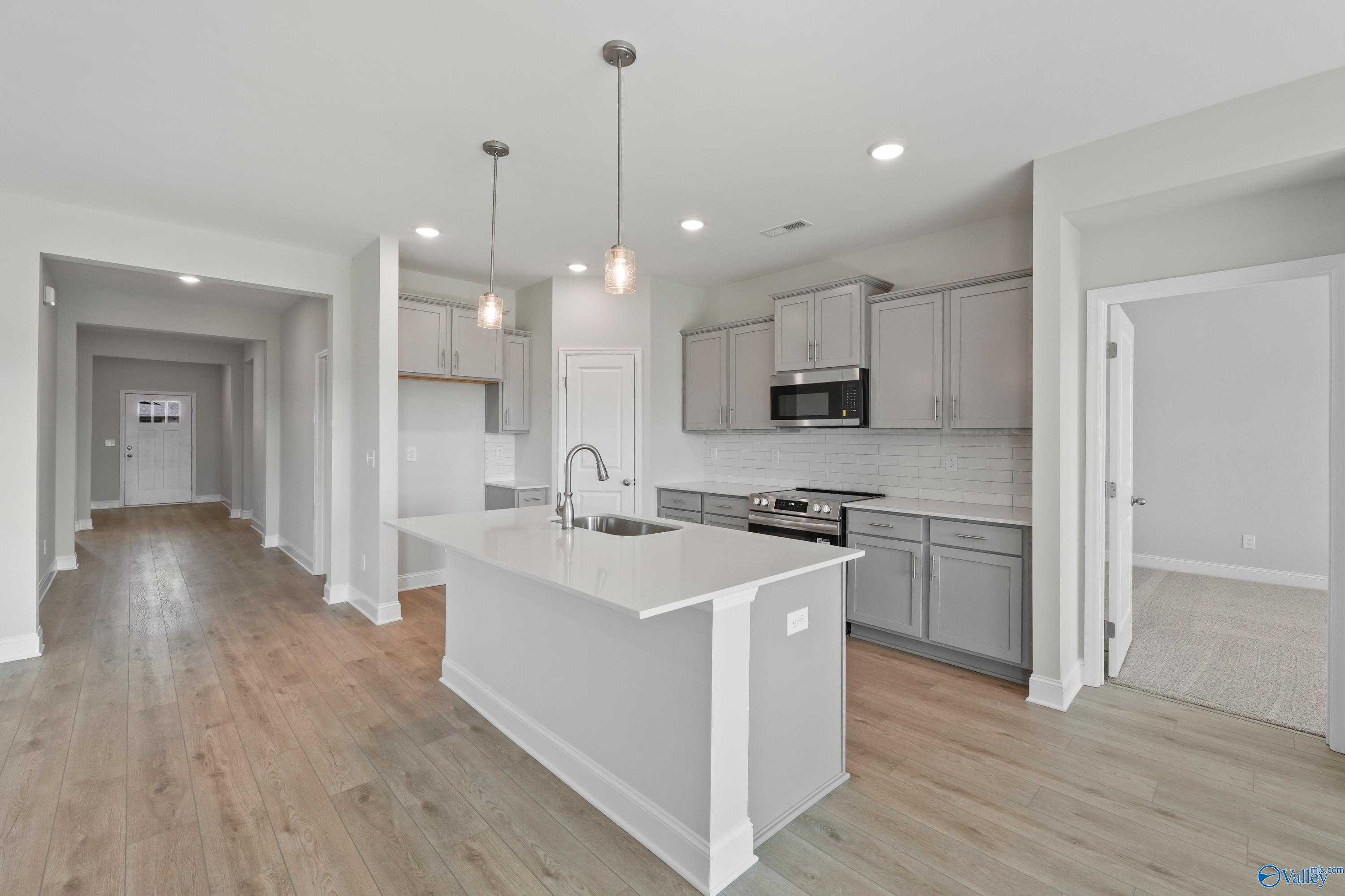Modern open-concept kitchen featuring white island, stainless appliances, and hardwood floors in The Everett by Davidson Homes, Hazel Green, AL