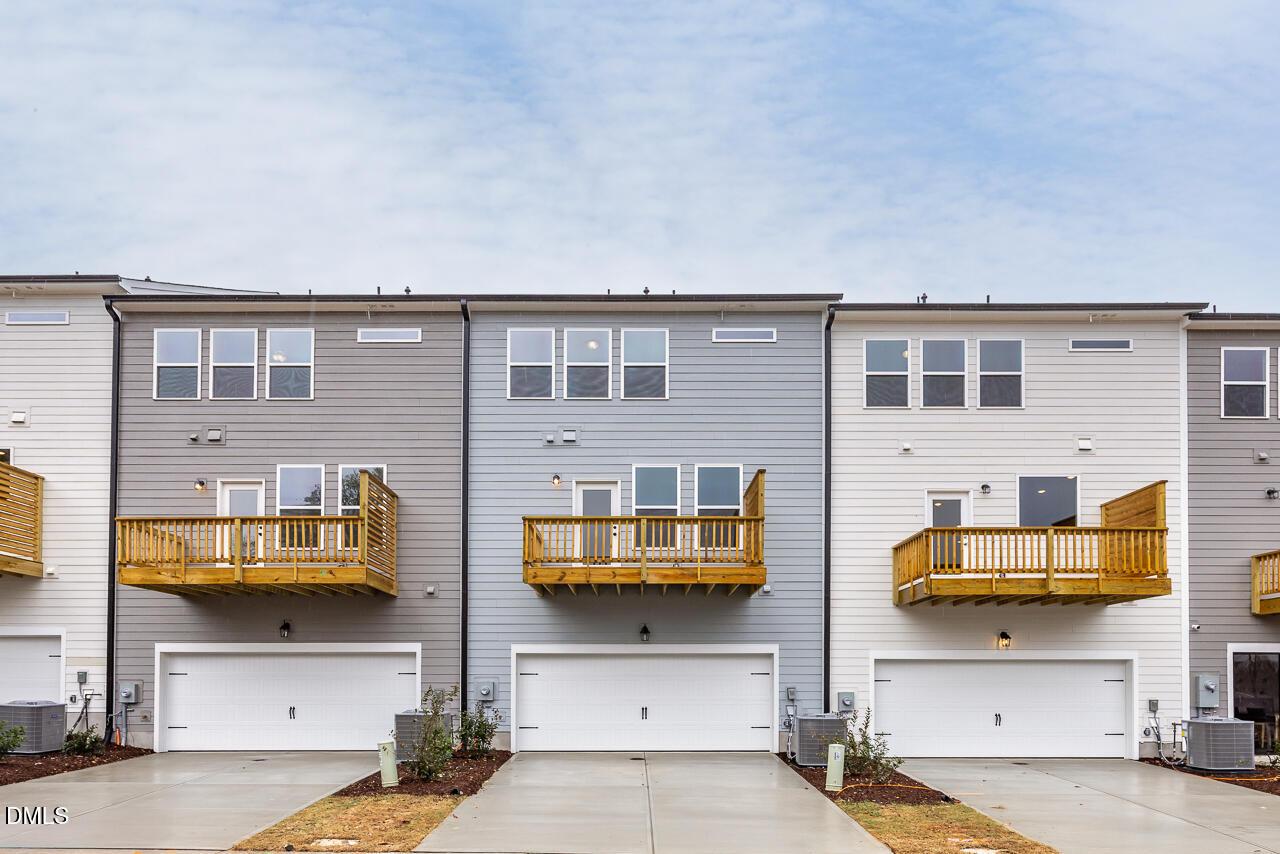 Row of modern 3-story townhomes with wooden balconies, two-car garages, and gray-white siding in Camden Park, Knightdale, NC