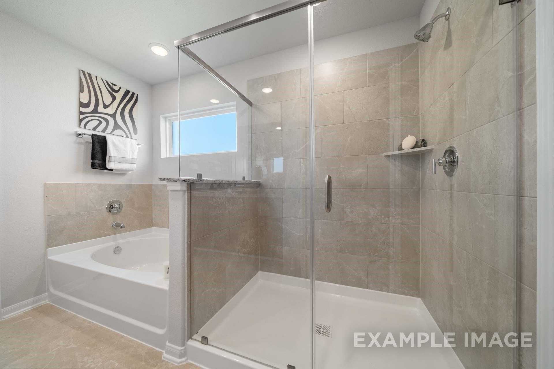 Modern master bathroom with frameless glass shower, soaking tub, and neutral tile in Davidson Homes Acadia A, Lago Mar, Texas