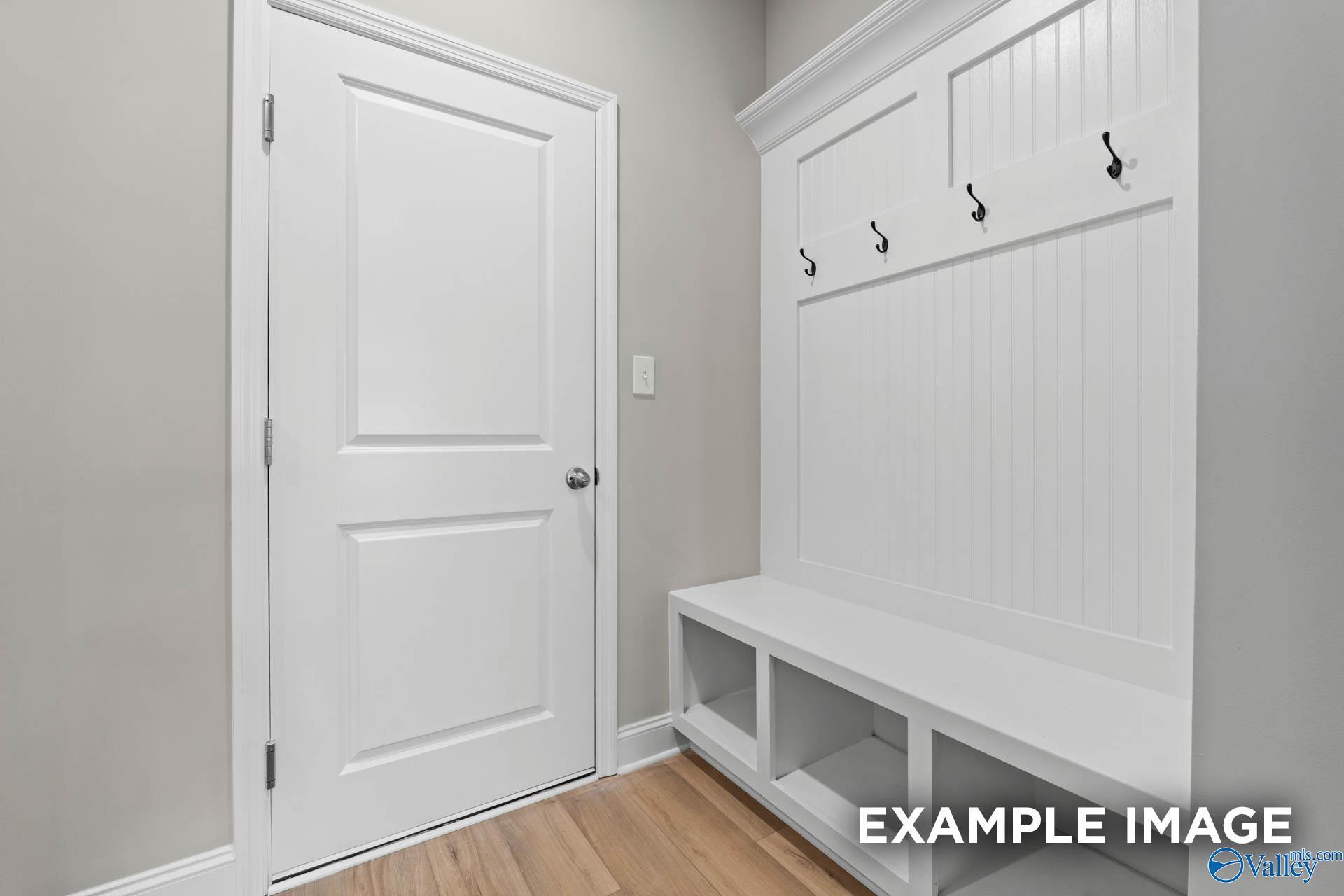 White mudroom with built-in bench, hooks, and cubbies beside open door in Davidson Homes The Finleigh, Harvest, Alabama