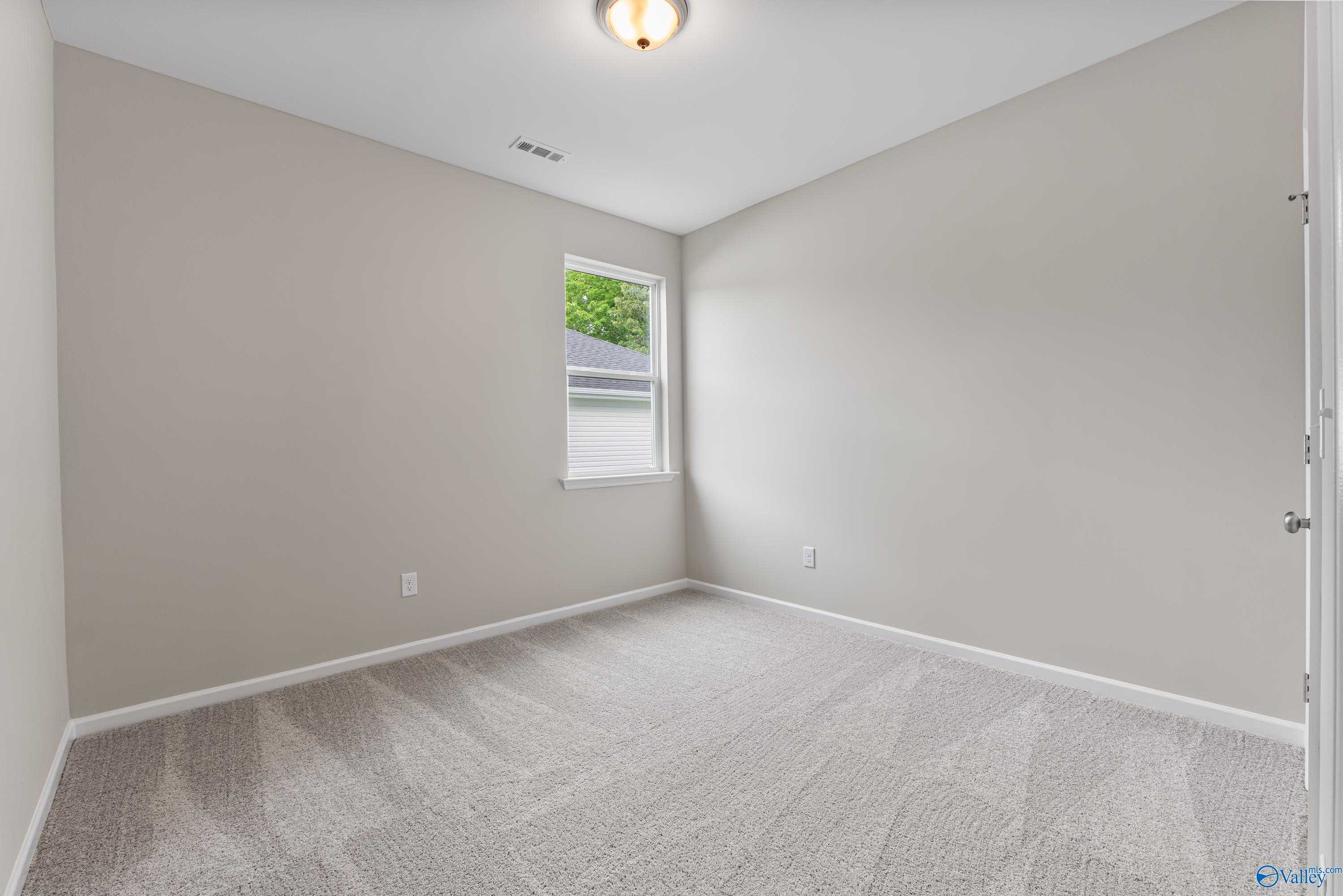 Bright secondary bedroom with neutral gray walls, beige carpet, and window view in The Phoenix by Davidson Homes, Fayetteville, TN