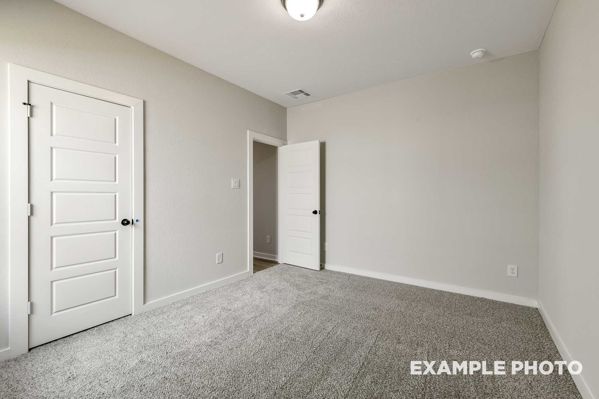 Spacious secondary bedroom in The Daphne G featuring neutral beige walls, gray carpet flooring, and white paneled doors