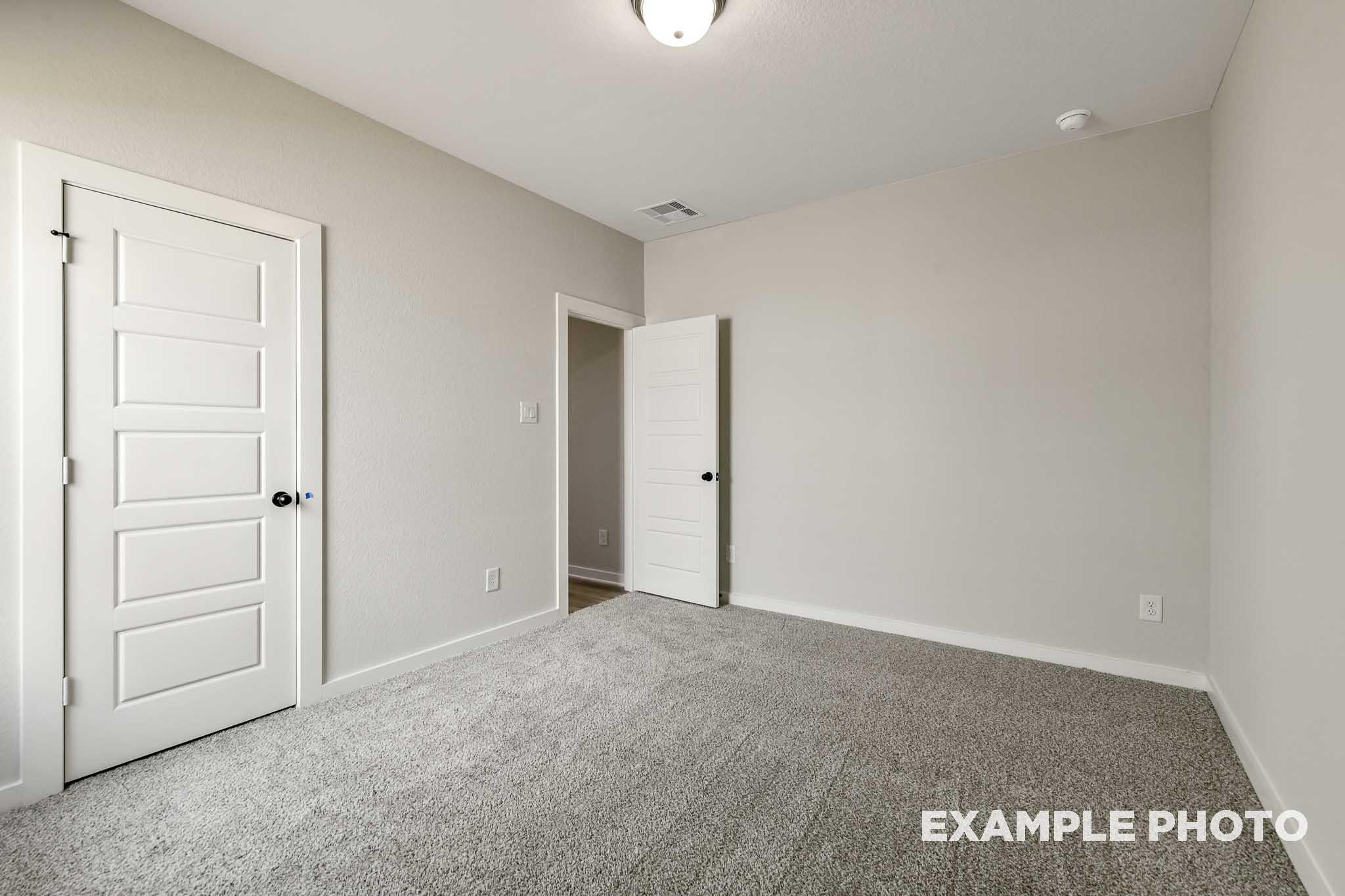 Spacious secondary bedroom in The Daphne G featuring neutral beige walls, gray carpet flooring, and white paneled doors