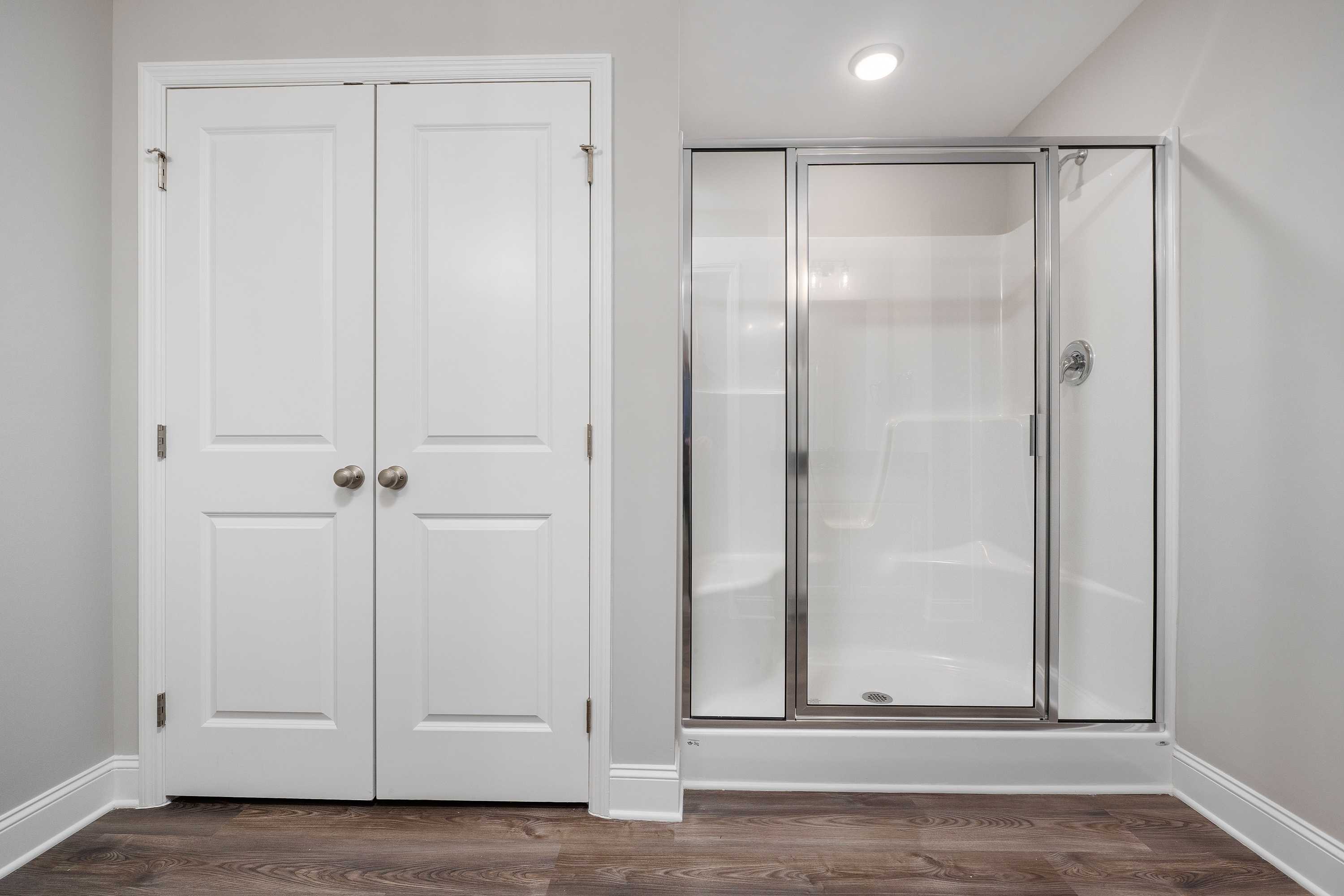 Master bathroom in The Aiken featuring white double-door walk-in closet and frameless glass shower enclosure