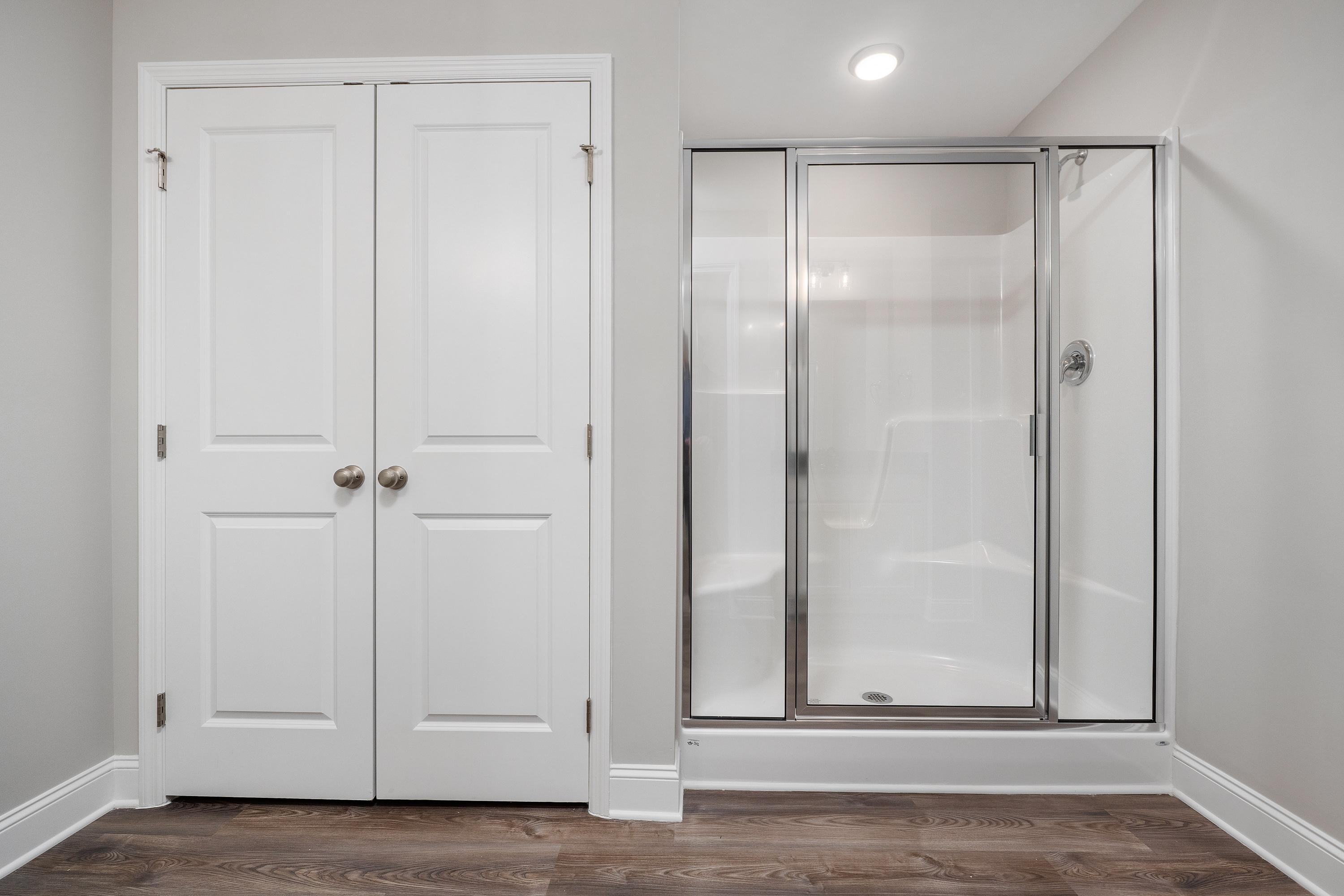 Master bathroom in The Aiken featuring white double-door walk-in closet and frameless glass shower enclosure