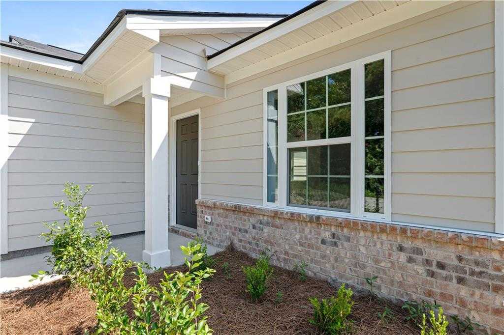 Charming single-story home exterior with beige siding, brick accents, covered porch, large window, and front landscaping in Phenix City, Alabama