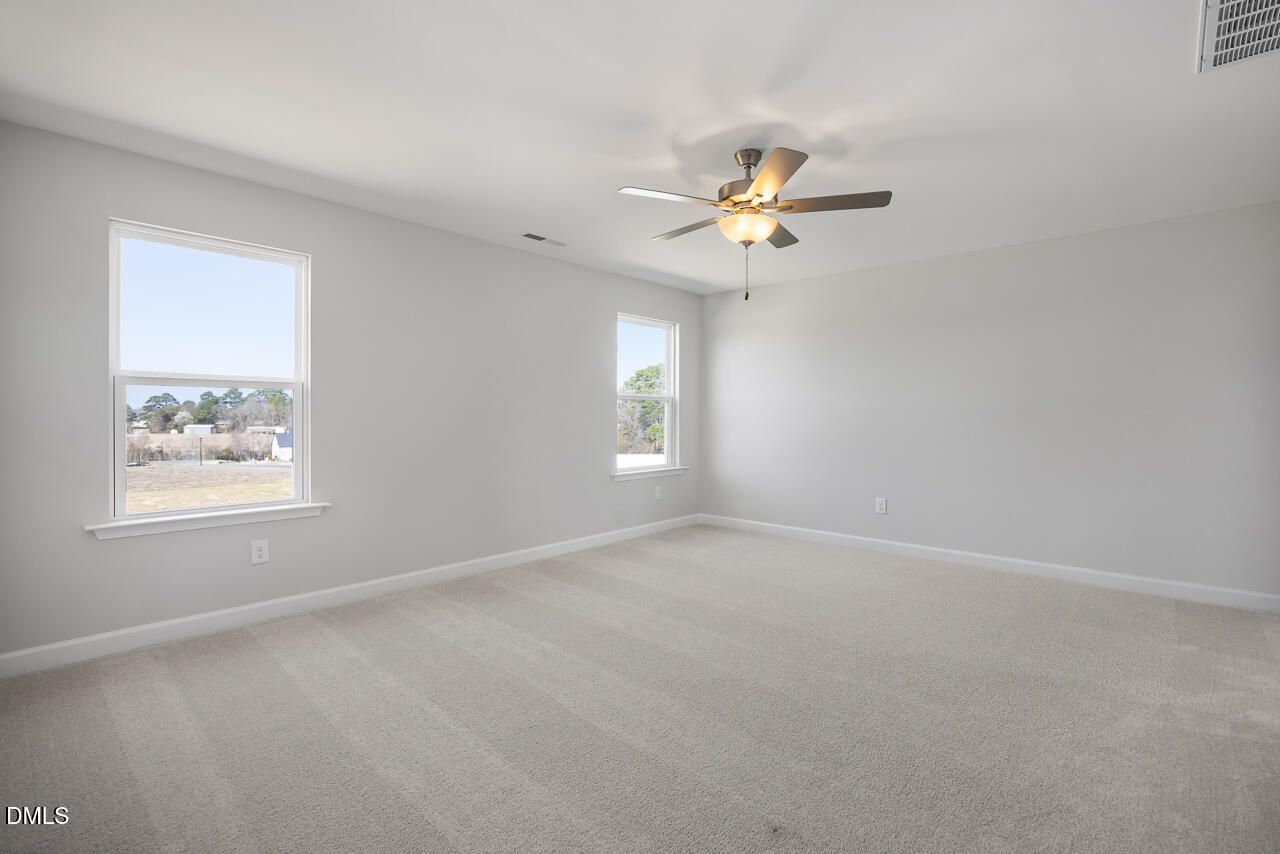 Spacious secondary bedroom with gray walls, beige carpet, ceiling fan, and large windows in Davidson Homes The Willow G, Angier, NC