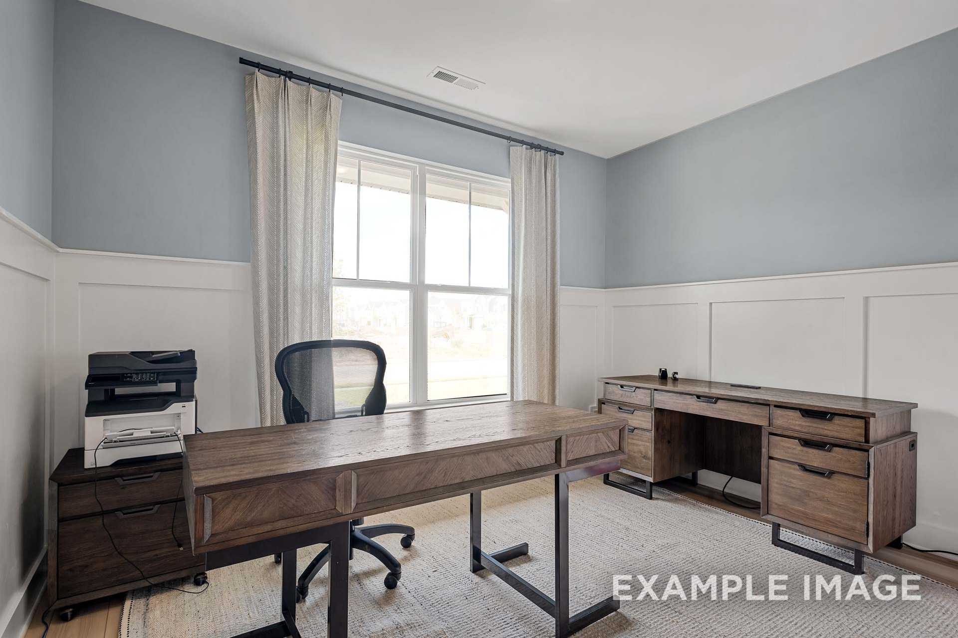 Spacious home office in The Ridgeport B with wooden L-desk, ergonomic chair, printer, and large windowed walls