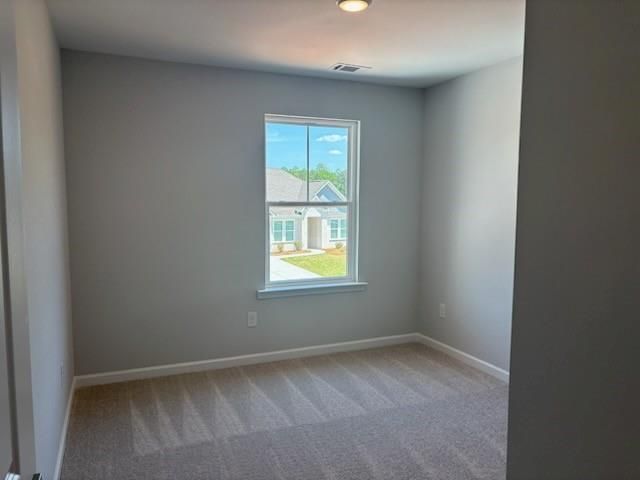 Empty secondary bedroom with light gray walls, beige carpet, and large window overlooking backyard in Davidson Homes The Rabun A, Winder, Georgia
