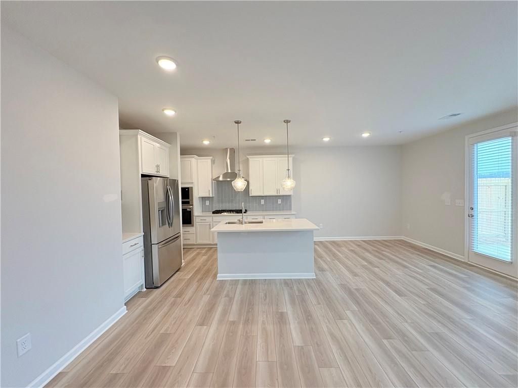 Modern open kitchen with white island, stainless steel appliances, and light hardwood floors in The Wake E floor plan, Cumming, GA