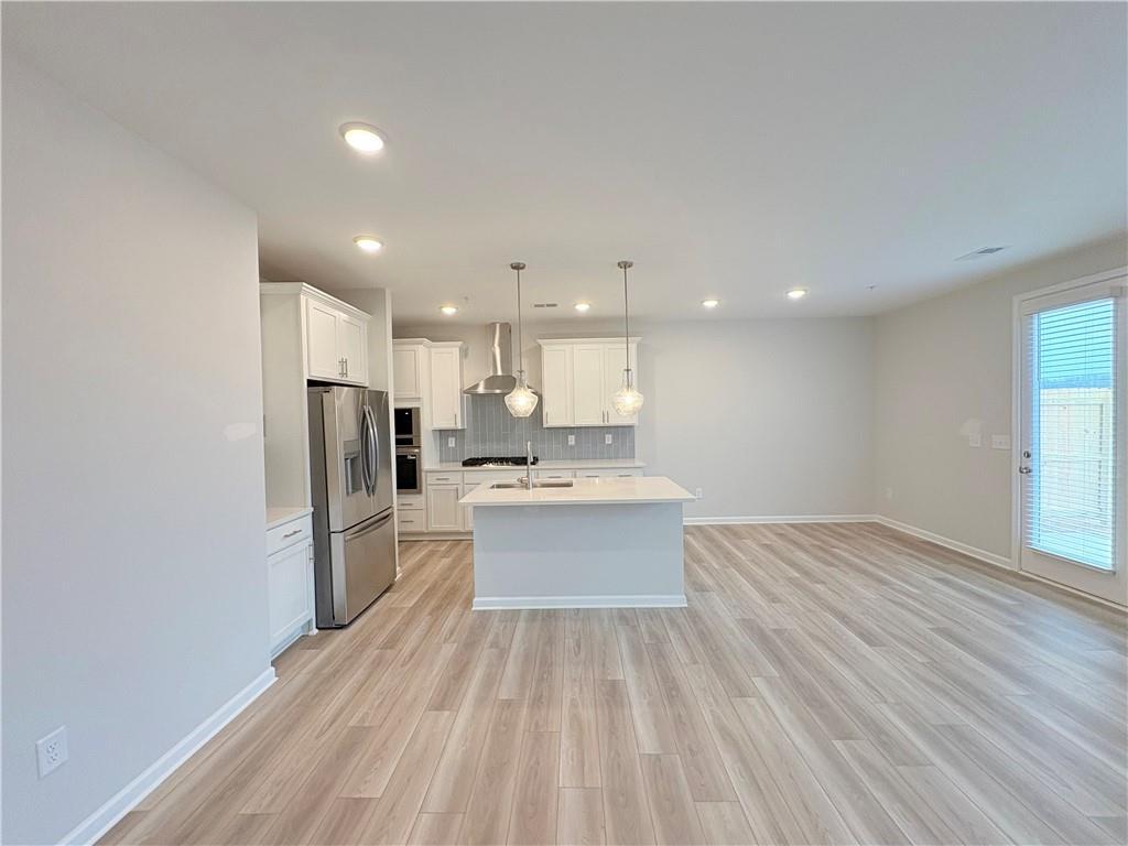 Modern open kitchen with white island, stainless steel appliances, and light hardwood floors in The Wake E floor plan, Cumming, GA