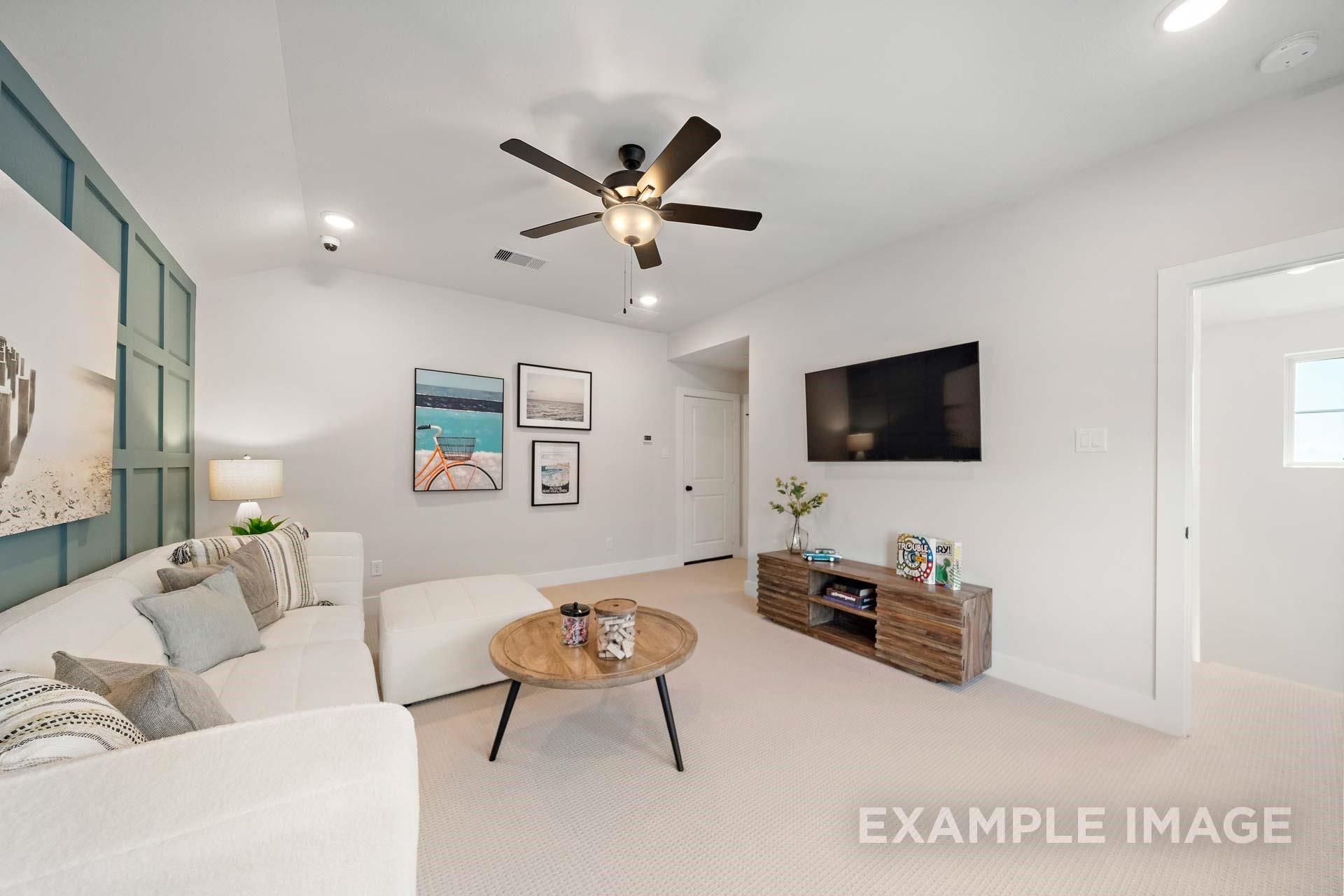 Cozy living room with white L-shaped sofa, wooden coffee table, mounted TV, beach wall art, and ceiling fan in Davidson Homes The Edward A, Lago Mar
