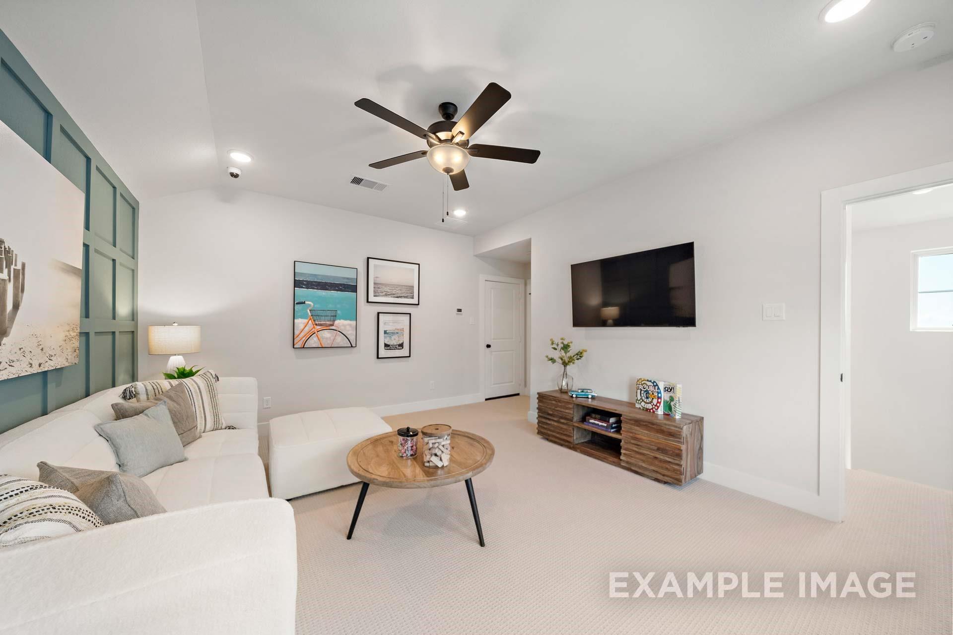 Cozy living room with white L-shaped sofa, wooden coffee table, mounted TV, beach wall art, and ceiling fan in Davidson Homes The Edward A, Lago Mar