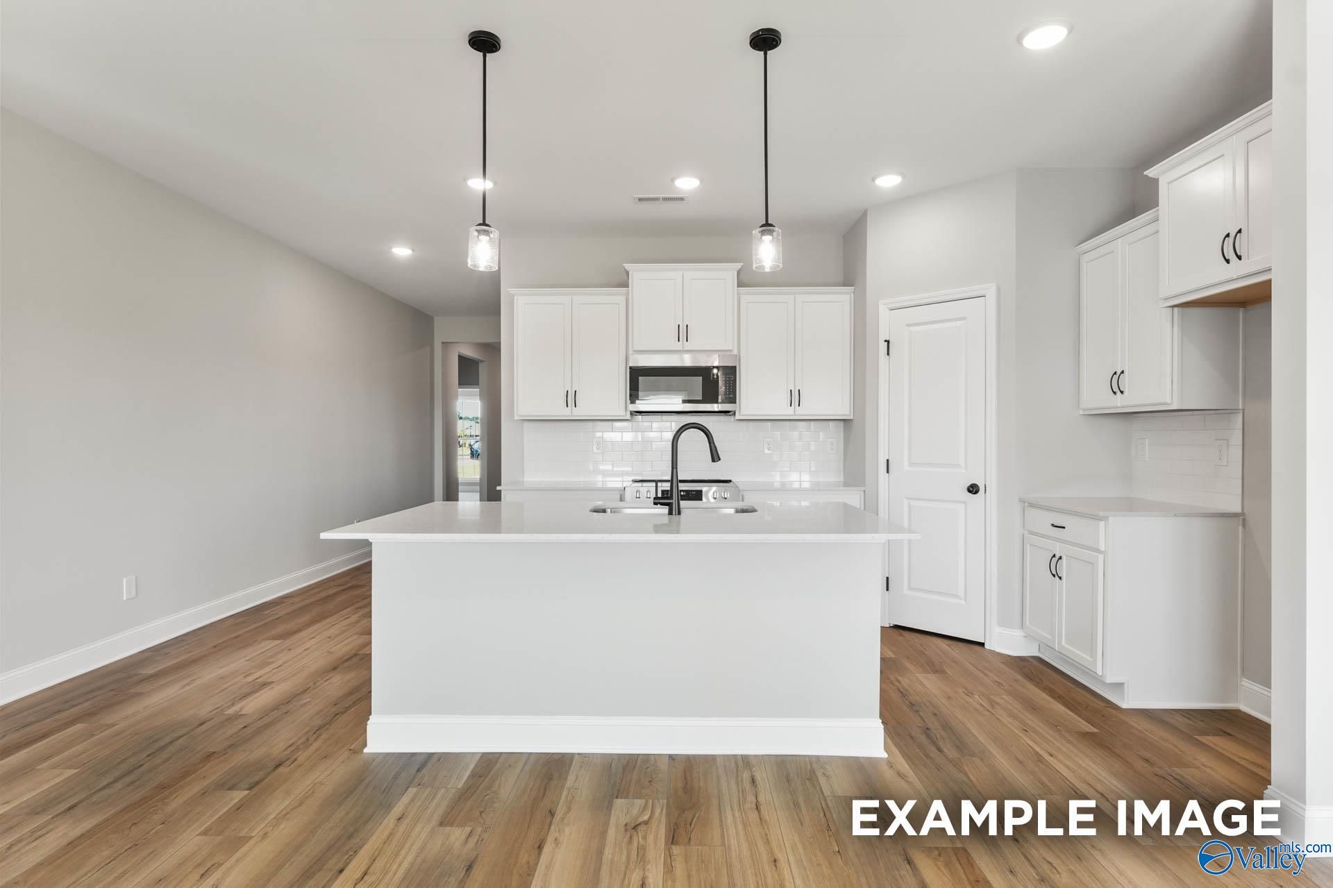 Bright open-concept kitchen with white cabinets, large island, stainless sink, and hardwood floors in Davidson Homes The Daphne C, Athens AL