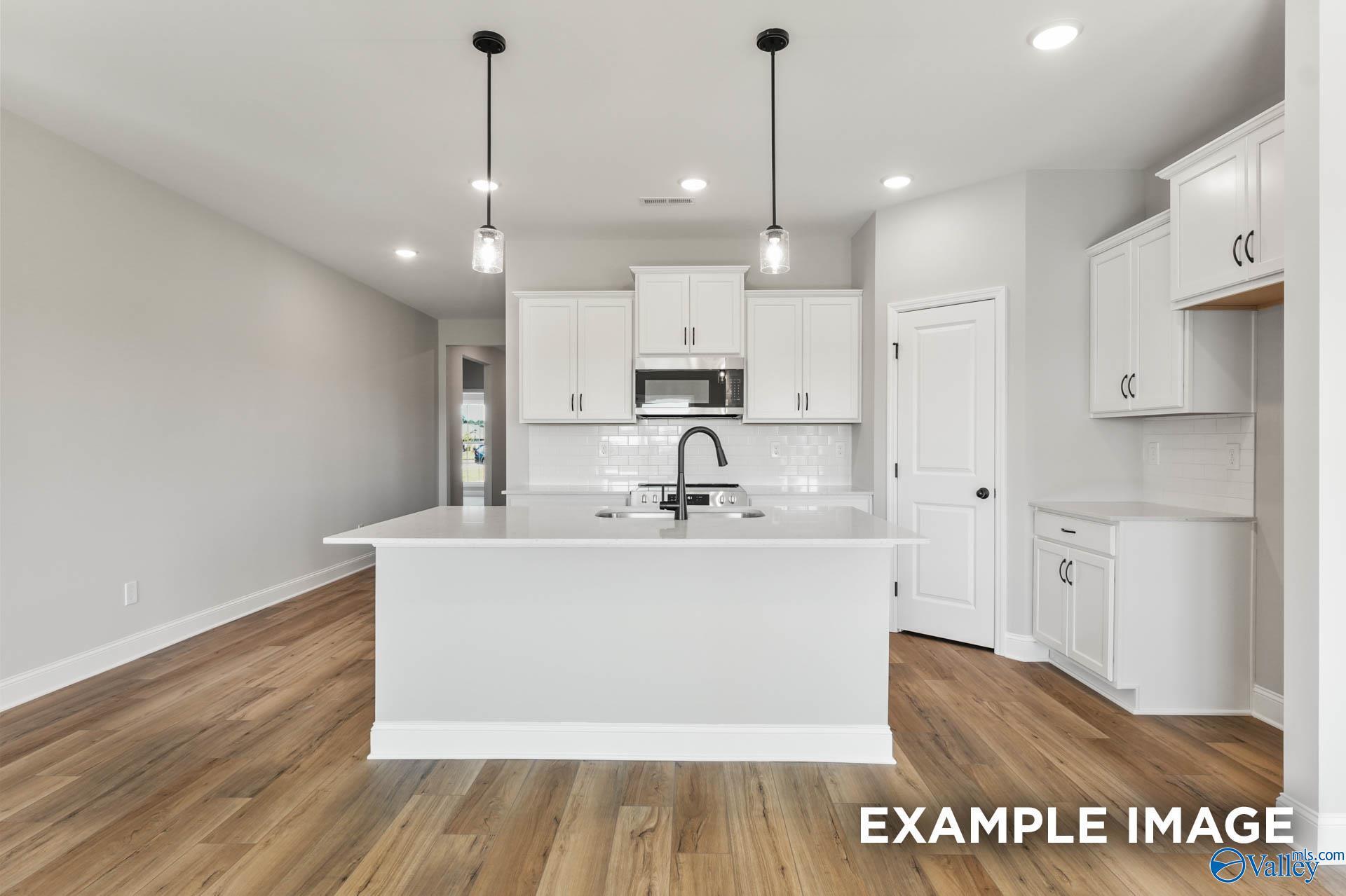 Bright kitchen with white cabinetry, center island, and pendant lights in Davidson Homes The Daphne C, Wood Trail, Toney, Alabama