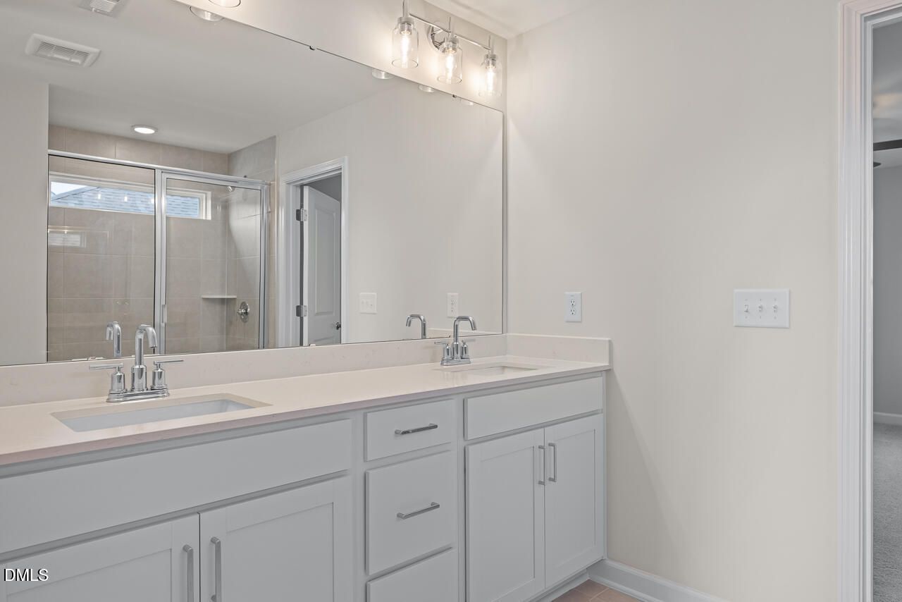 Double vanity bathroom with white cabinets, large mirror, and tiled walk-in shower in Davidson Homes The Willow C, Zebulon NC