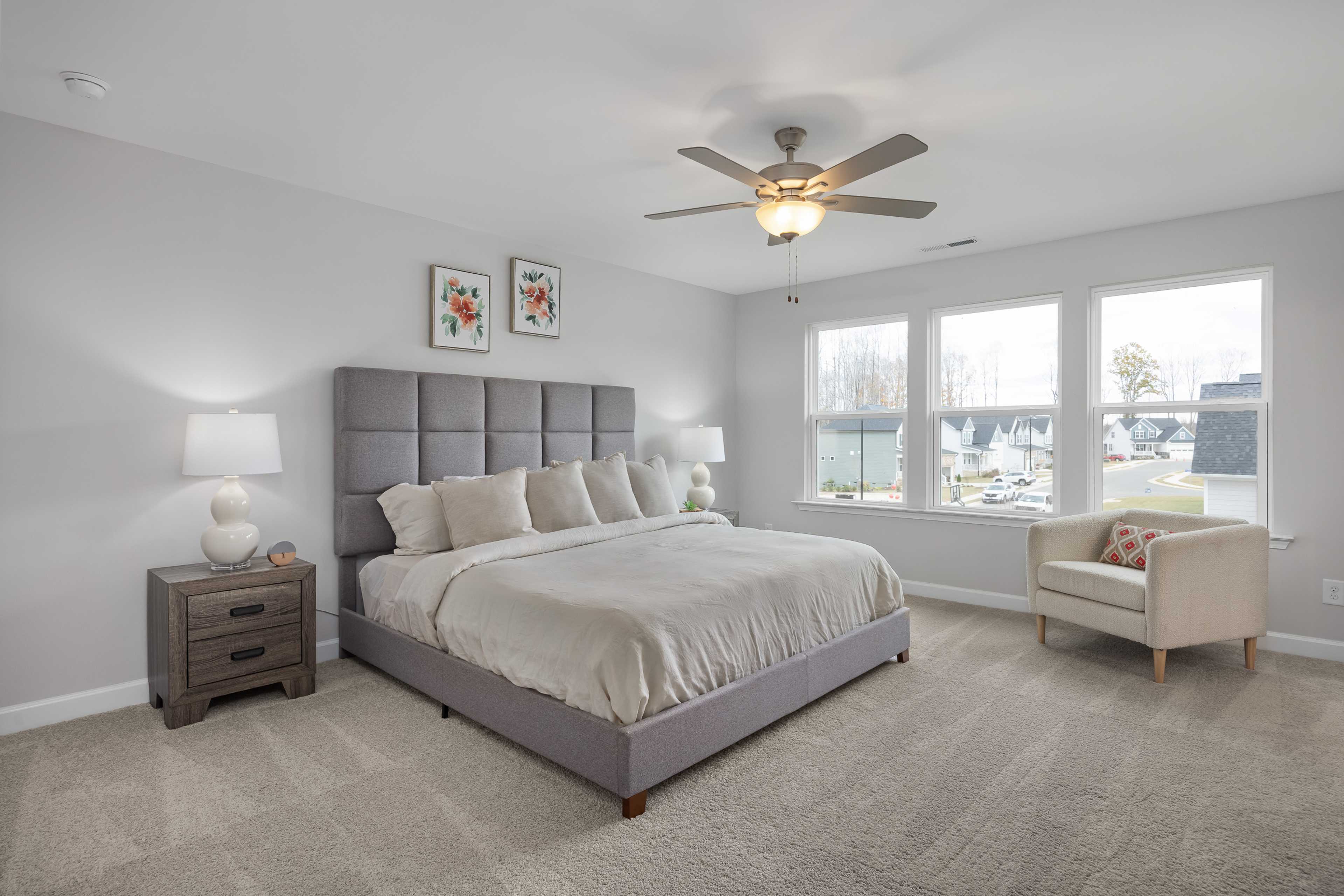 Modern primary bedroom at Enclave at Belmont in Belmont NC with gray upholstered king bed, ceiling fan, and scenic lake views