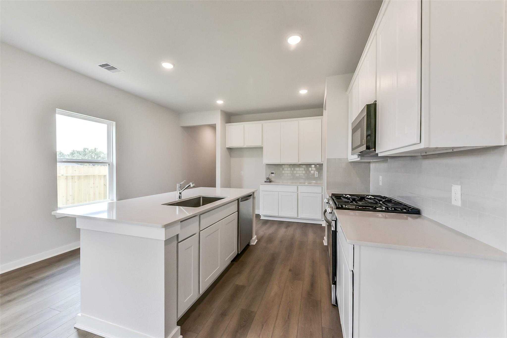 Modern white kitchen with quartz island, stainless appliances, and hardwood floors in Davidson Homes The Frio F, Dayton, Texas