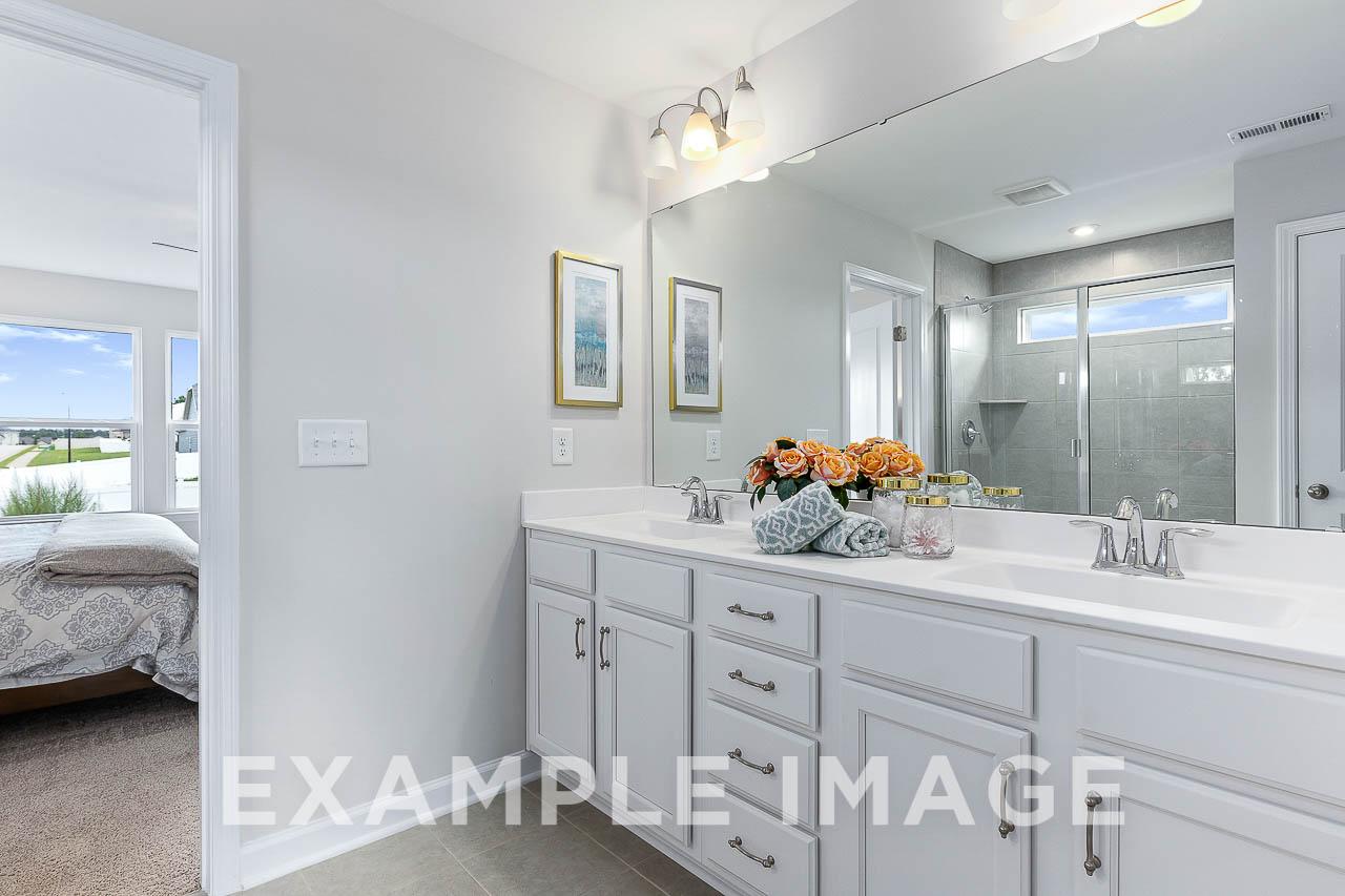 Spacious master bathroom in The Willow C home with double vanity, large mirror, walk-in shower, and bedroom view