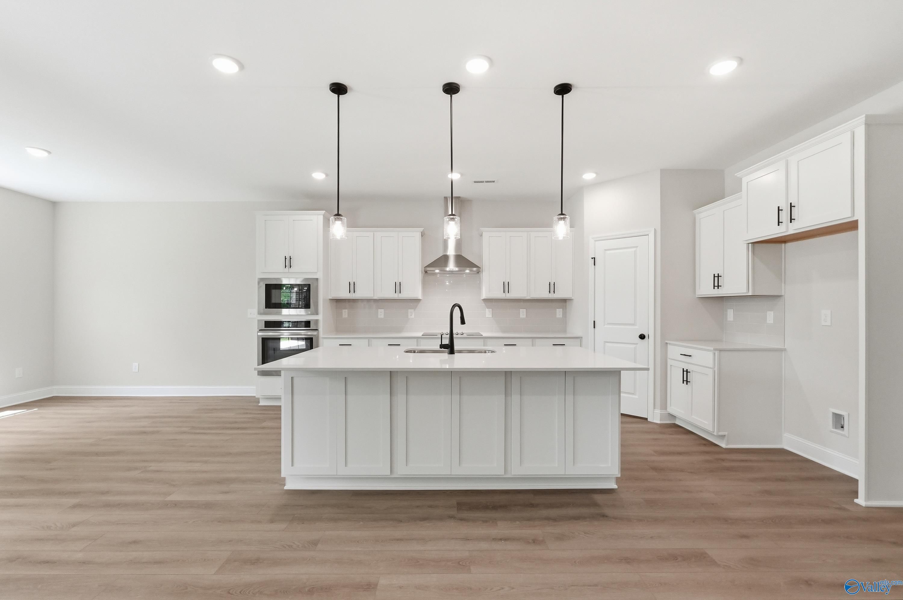 Modern white kitchen with central island, stainless steel appliances, and pendant lights in Davidson Homes The Rockford B, Athens, Alabama