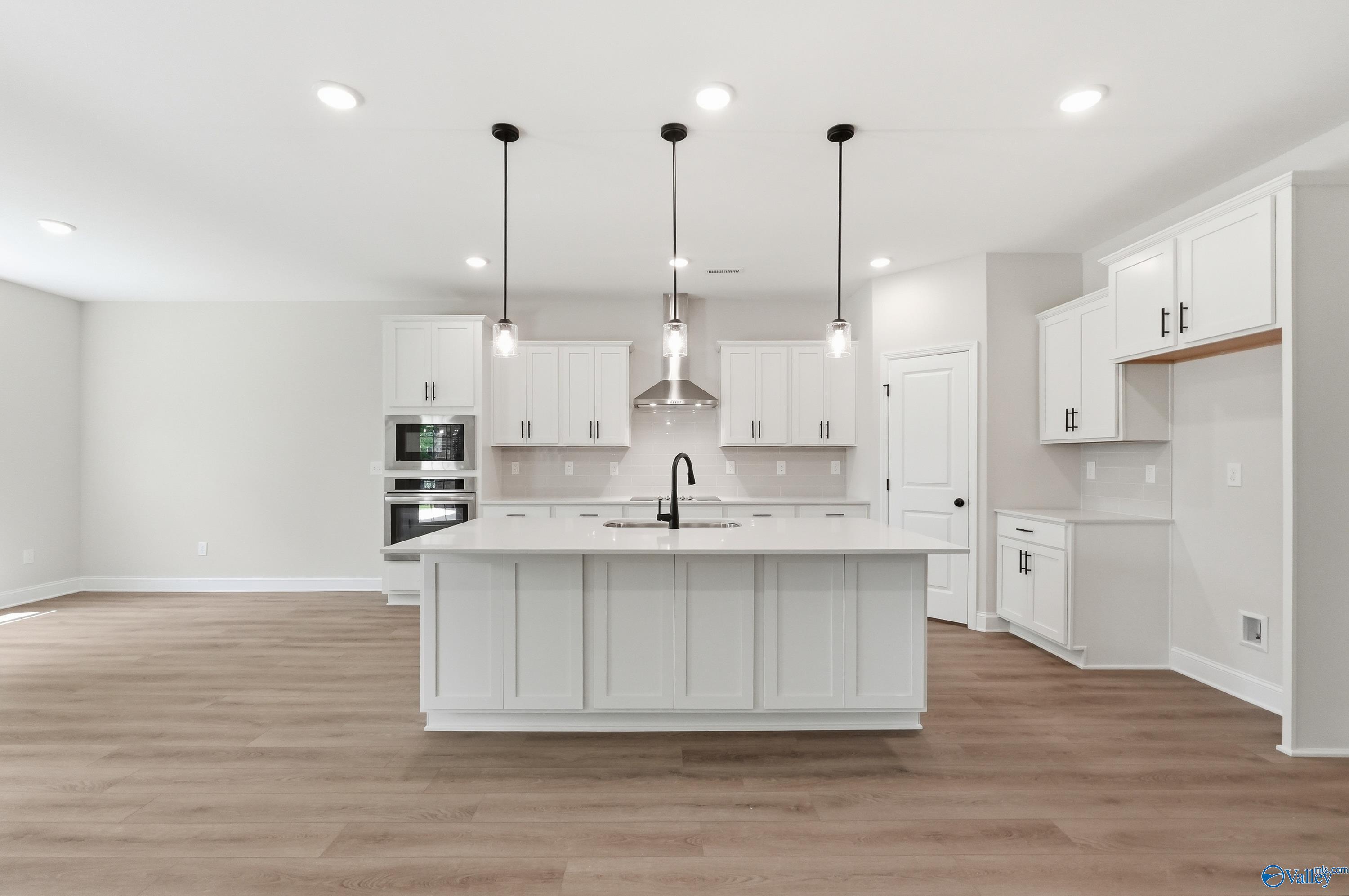 Modern white kitchen with large island and pendant lighting in The Rockford B floor plan at The Meadows in Athens, Alabama.