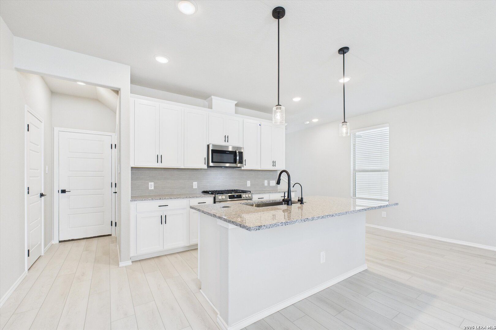Modern white kitchen with granite island, stainless microwave, gas cooktop, and pendant lights in Davidson Homes The Charlotte A, San Antonio