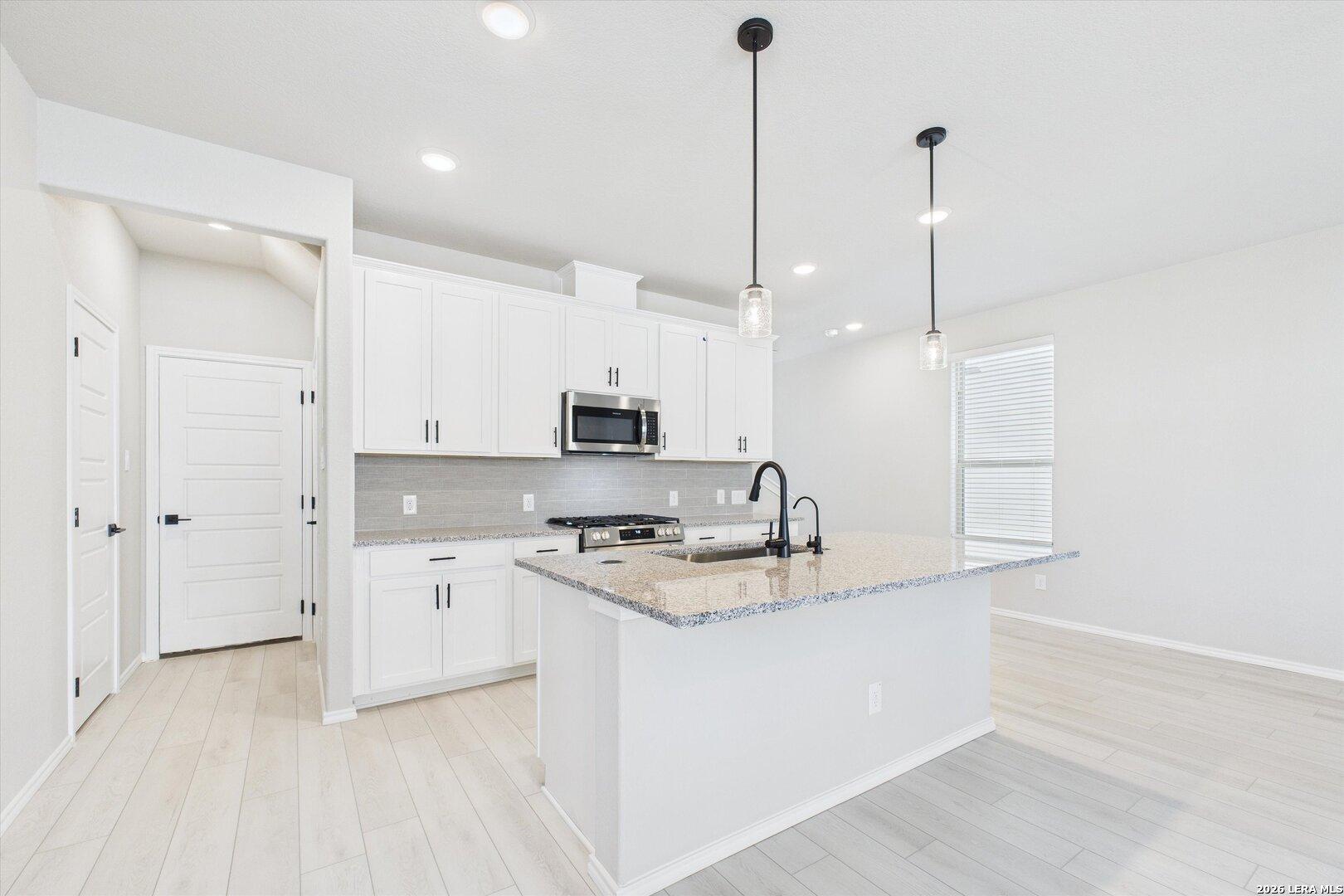 Modern white kitchen with granite island, stainless microwave, gas cooktop, and pendant lights in Davidson Homes The Charlotte A, San Antonio
