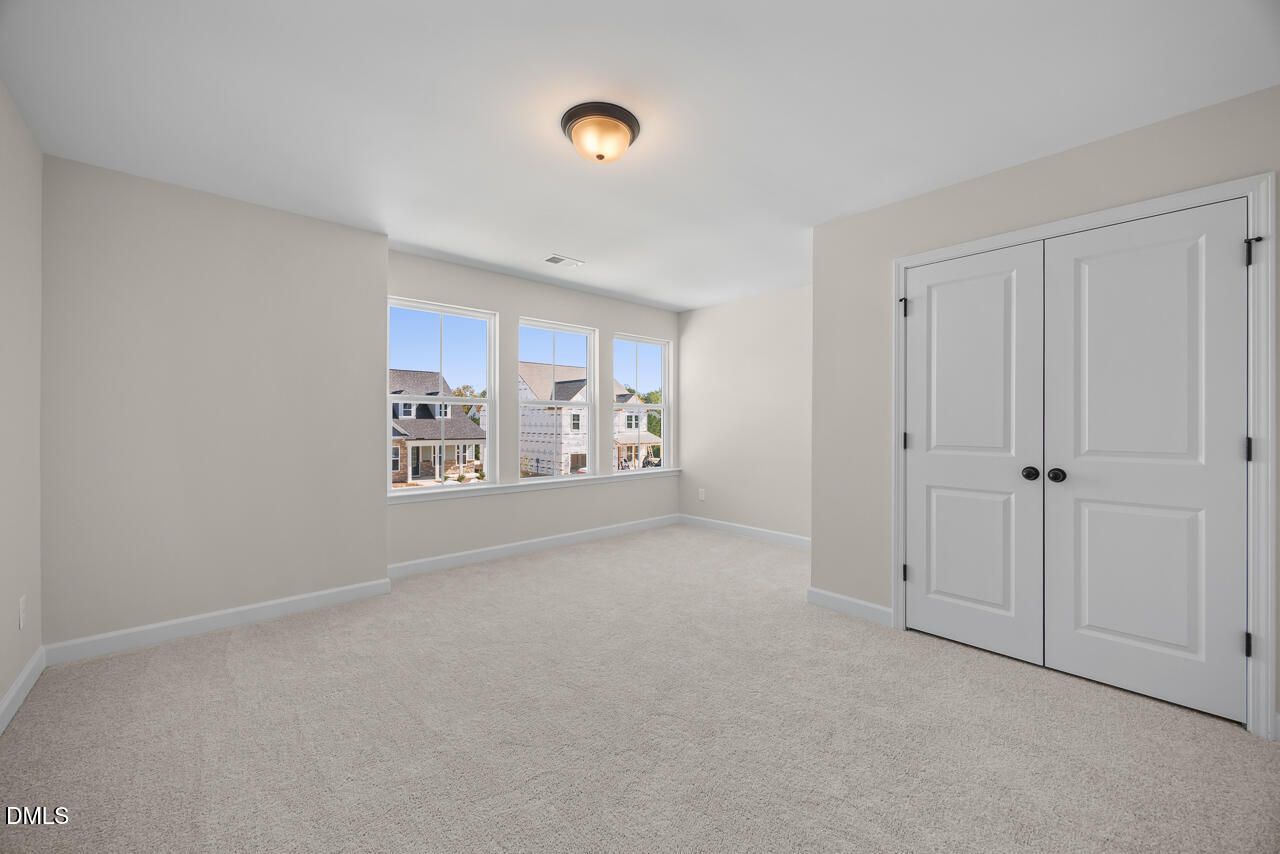 Bright bedroom with plush carpet, white double-door closet, and windows overlooking homes in Wendell Ridge, Wendell, North Carolina