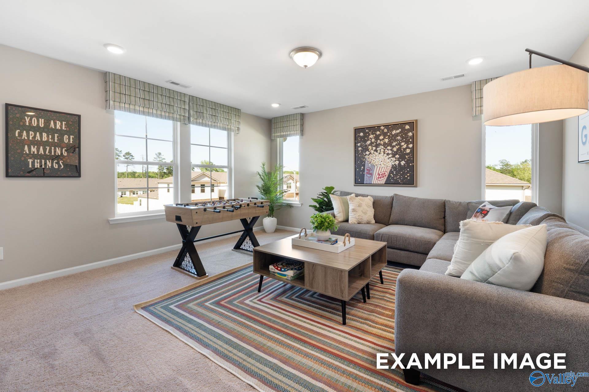 Cozy family room with gray L-shaped sofa, foosball table, modern art, and large windows in Davidson Homes The Stella, Madison, Alabama