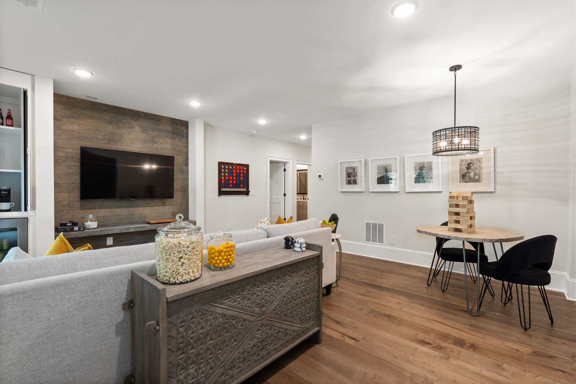Spacious open-concept living room in Tanglewood East Cobb GA with gray sectional sofa, hardwood floors, TV wall, game table and pendant lighting by Davidson Homes