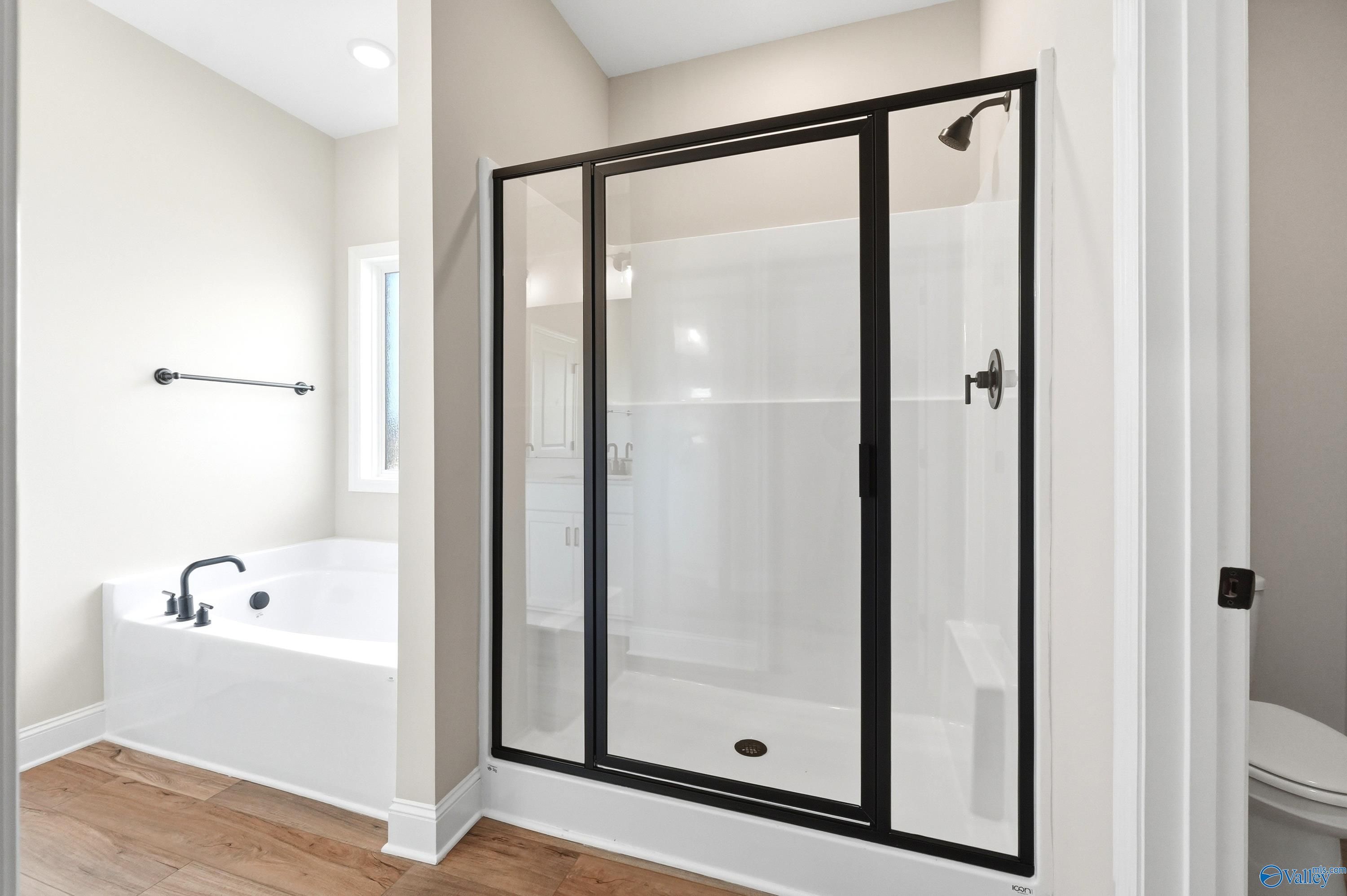 Modern master bathroom with glass-enclosed walk-in shower and soaking tub in The Daphne D floor plan, Harvest, Alabama.