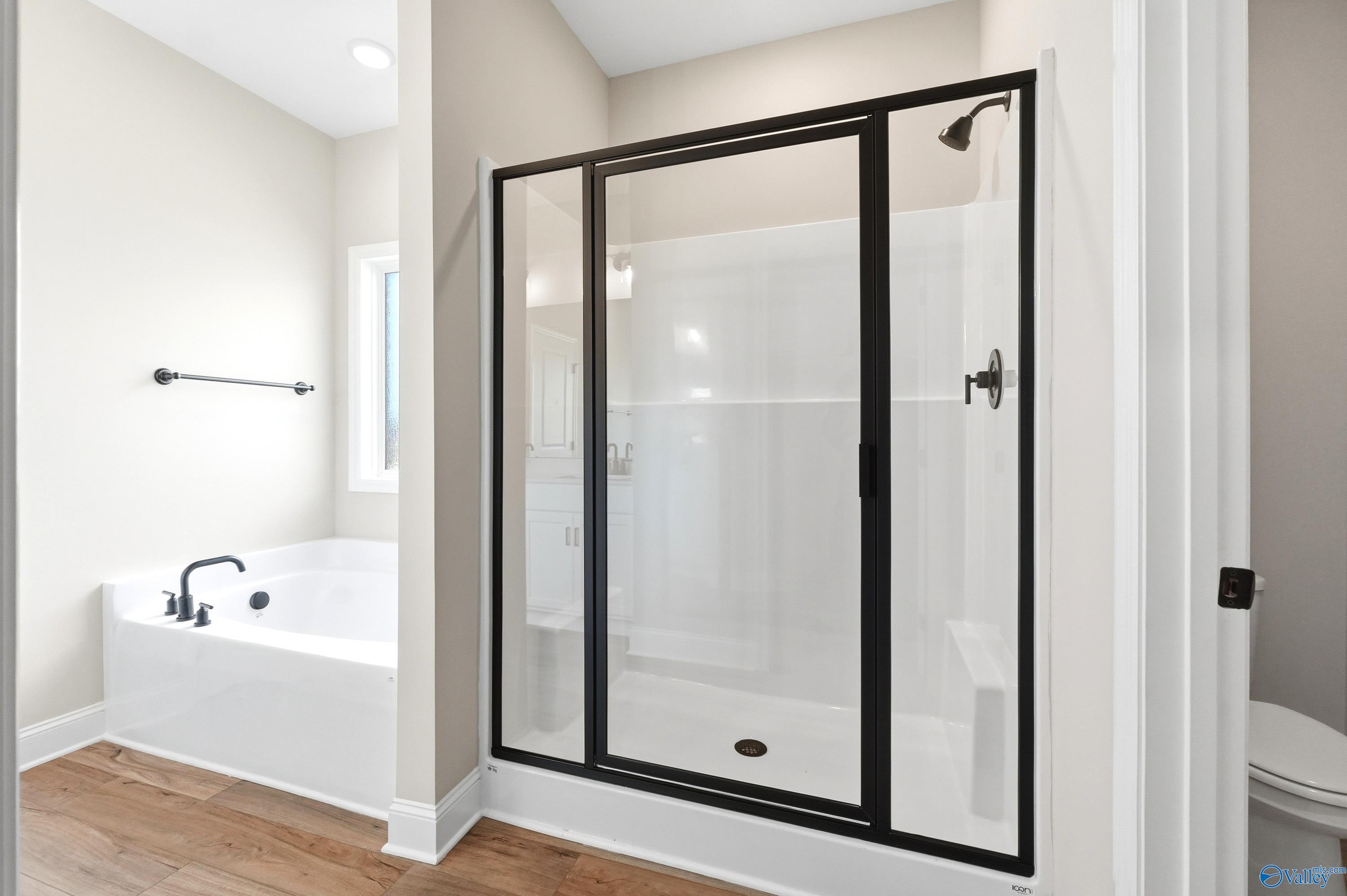 Modern master bathroom with glass-enclosed walk-in shower and soaking tub in The Daphne D floor plan, Harvest, Alabama.