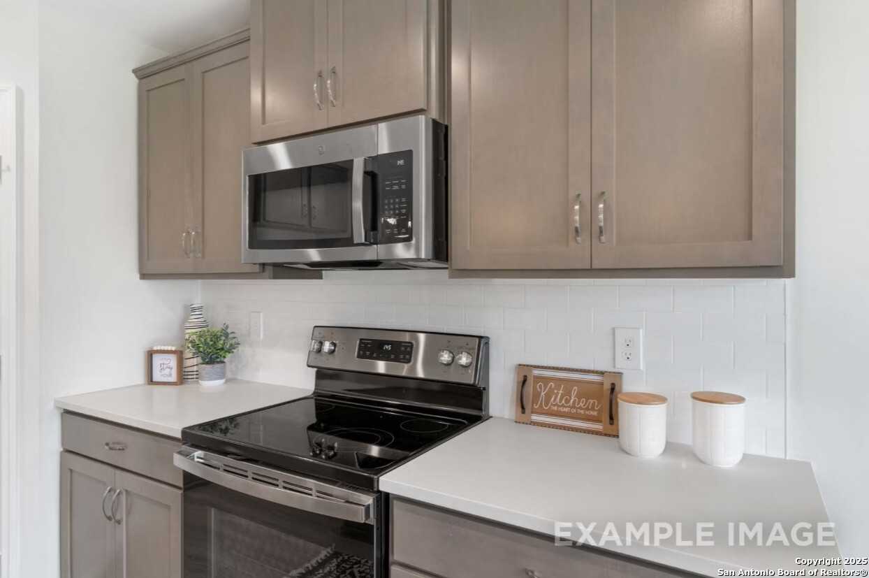 Modern kitchen featuring stainless steel microwave, oven, and cooktop with beige shaker cabinets in Davidson Homes The Asheville K, San Antonio