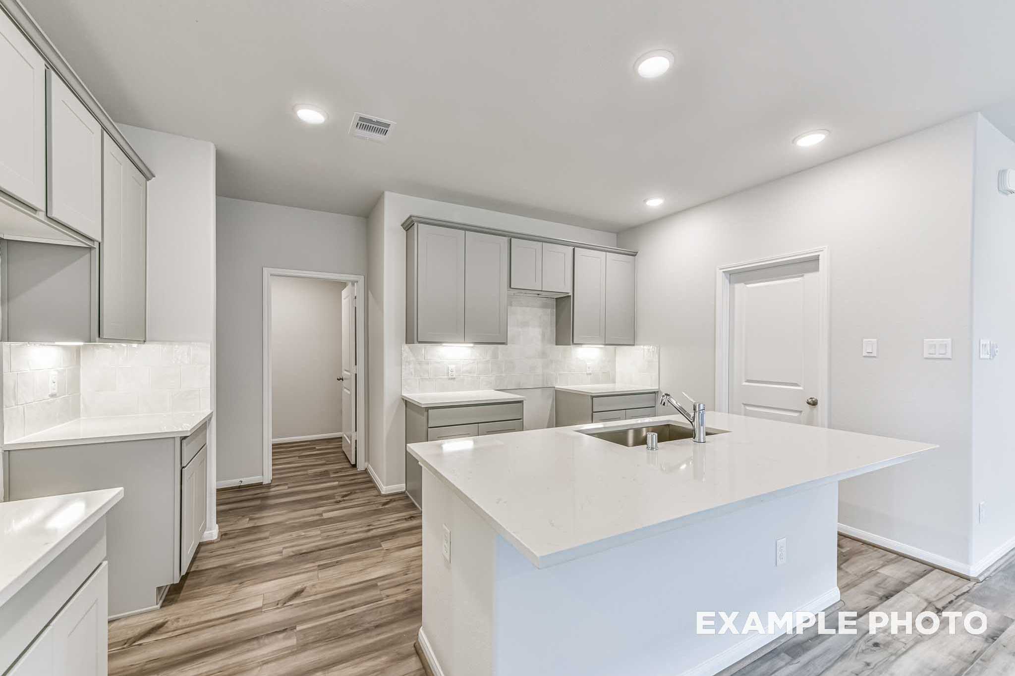 Contemporary kitchen in The Laguna A home with white shaker cabinets, quartz island sink, subway tile backsplash, and hardwood floors