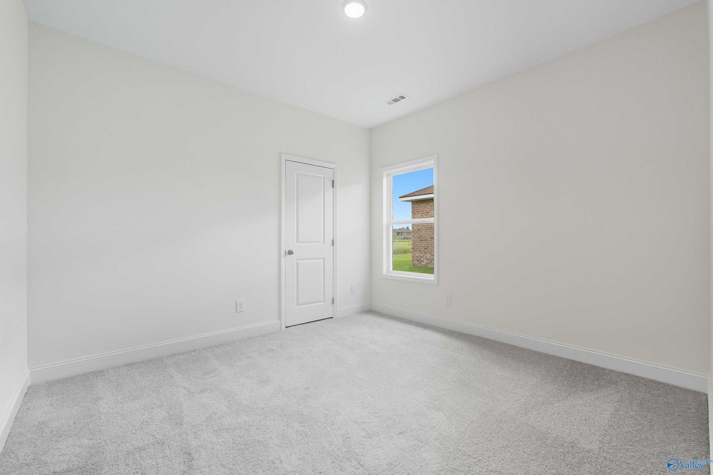 Bright secondary bedroom with neutral walls, plush gray carpet, and window view in Davidson Homes The Everett, Meridianville, Alabama