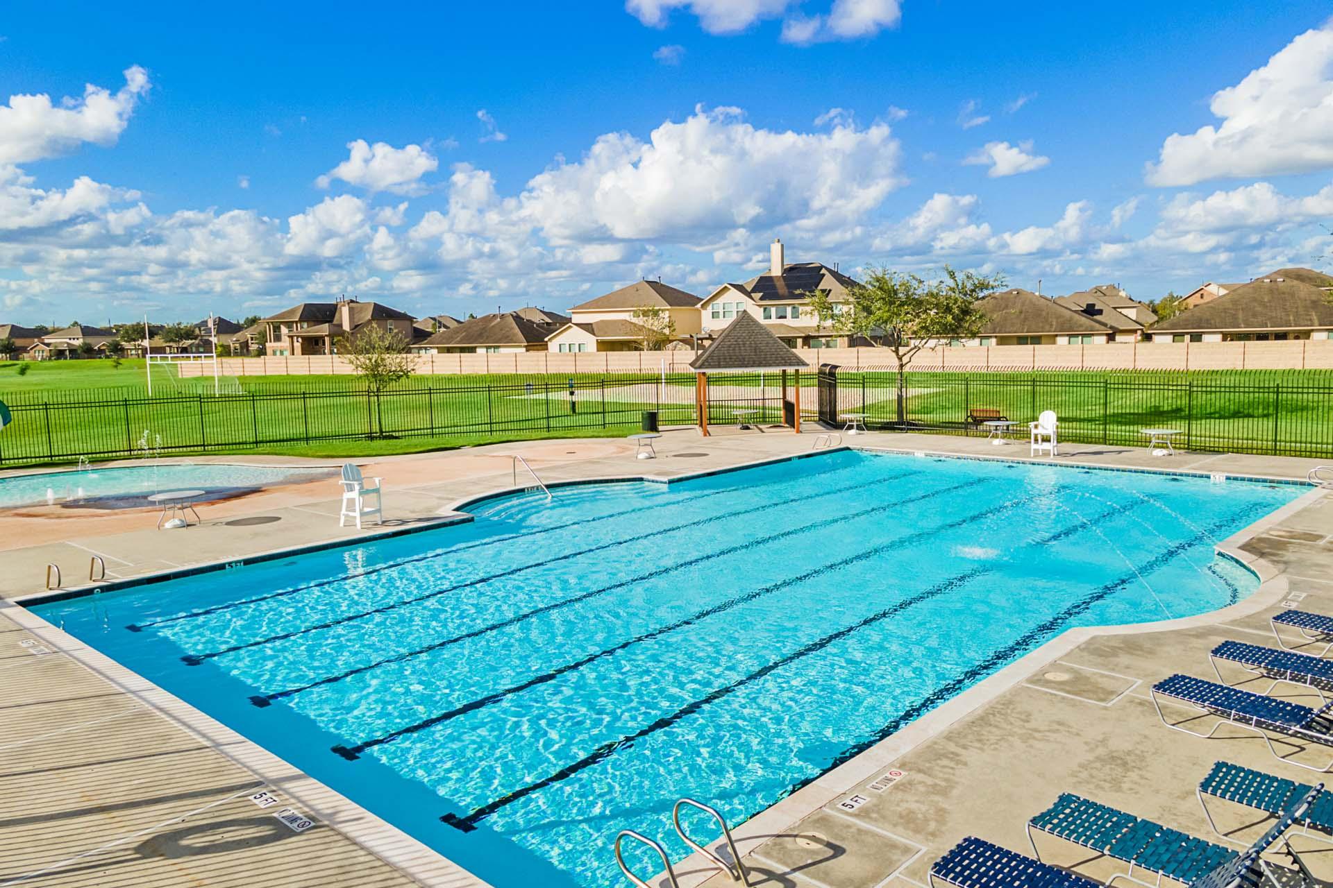 Resort-style lap pool at Sierra Vista in Rosharon Texas with hot tub lounge chairs and fenced green space
